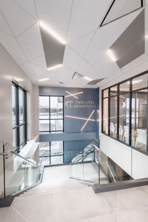 Modern interior stairwell at orthopedic surgery center with glass walls and blue accent wall.