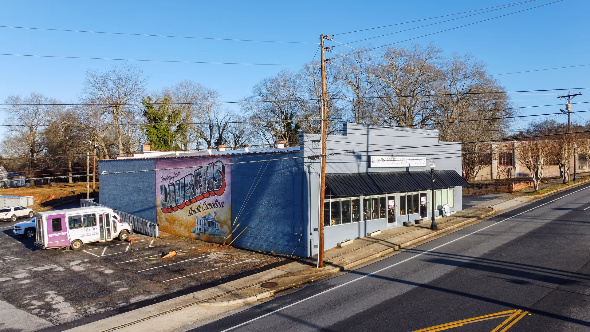 Blue storefront building along a street with parking and leafless trees.