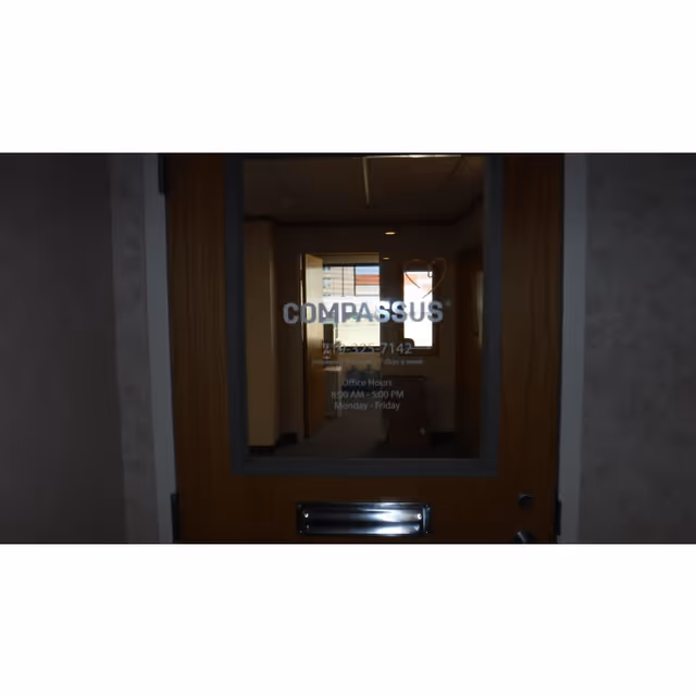 Door with Compassus logo and hallway visible through glass window.