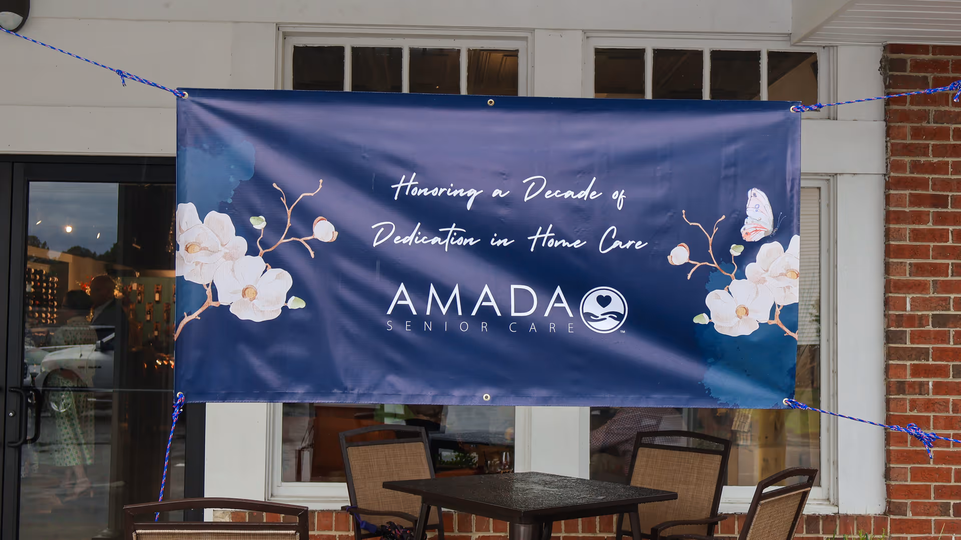 Blue Amada Senior Care banner hangs outside beside a patio table.