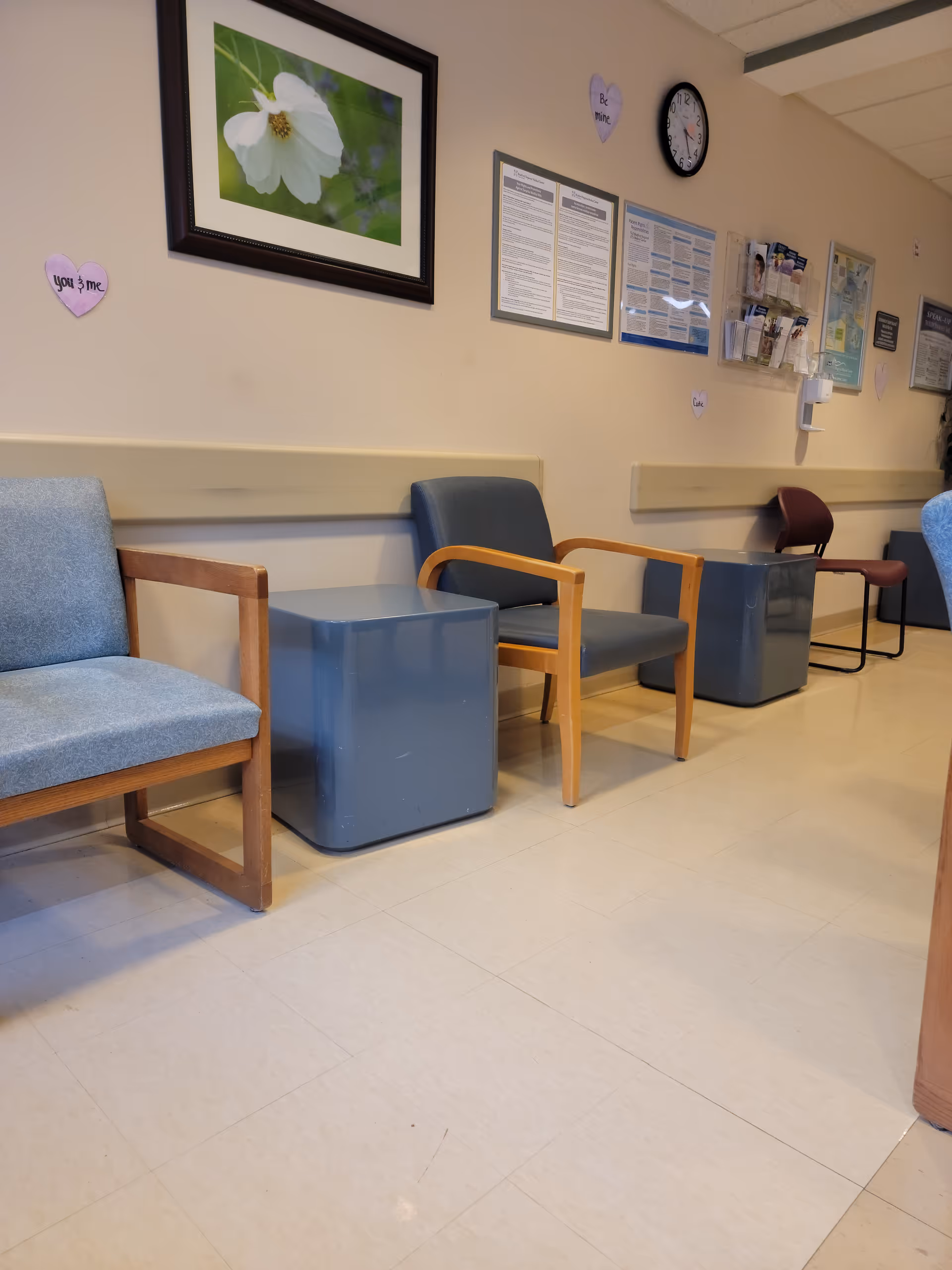 Waiting area in a medical facility with blue chairs, small tables, and wall posters.