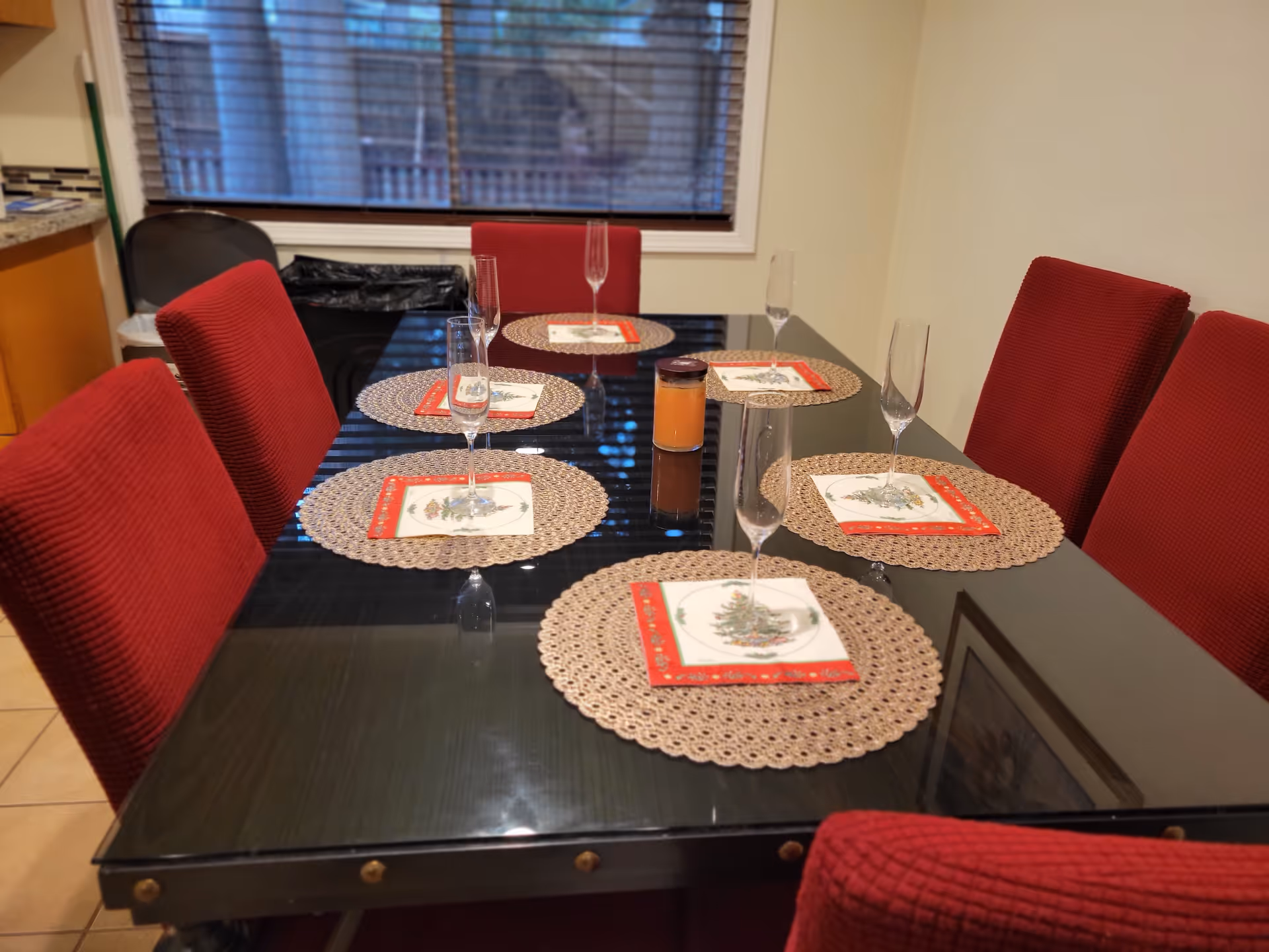 Rectangular glass dining table with red upholstered chairs and place settings in dining room.