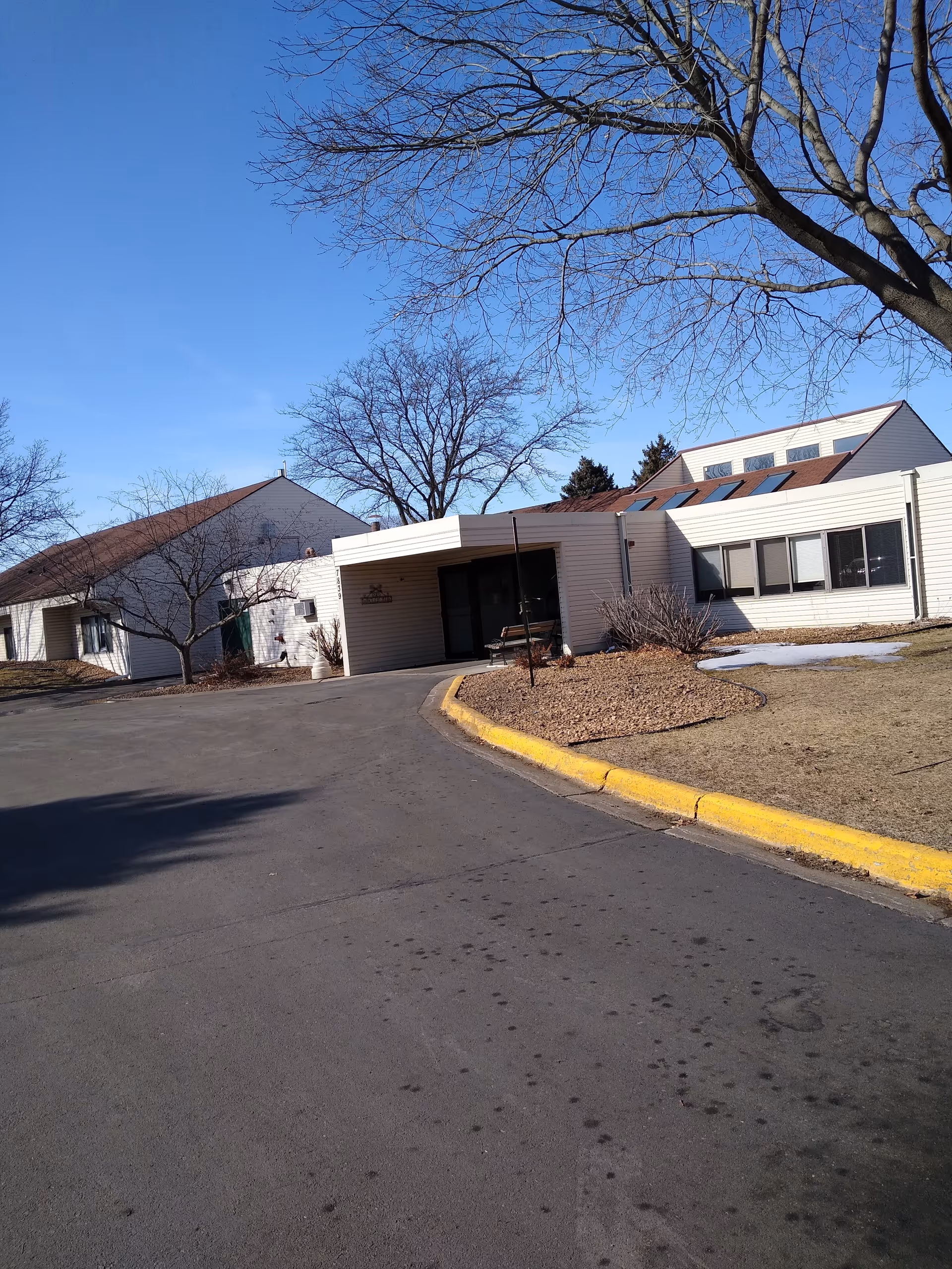 Exterior view of a senior living facility entrance with driveway and leafless trees.