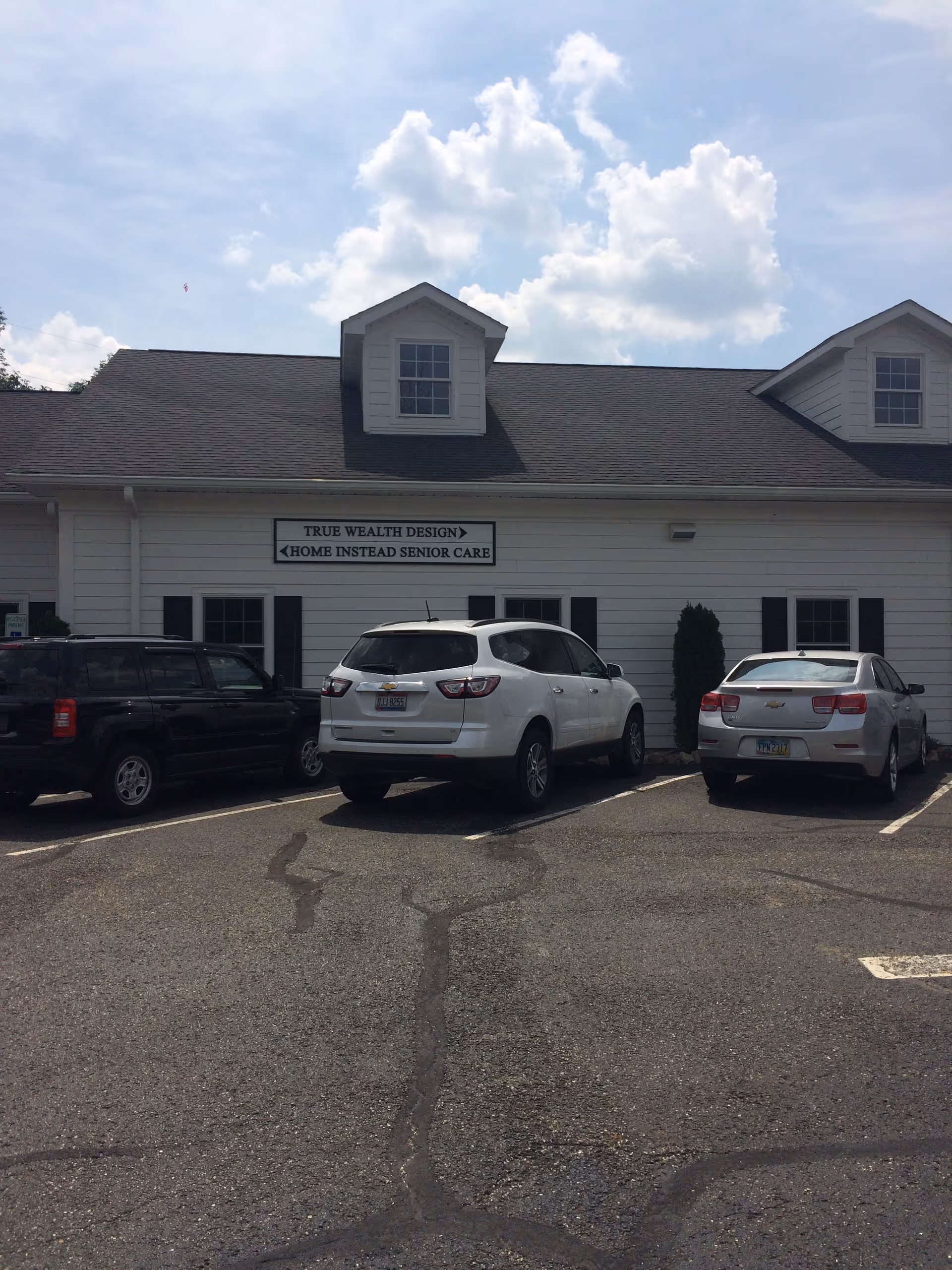 White, single-story building with a sign and parked cars in front.