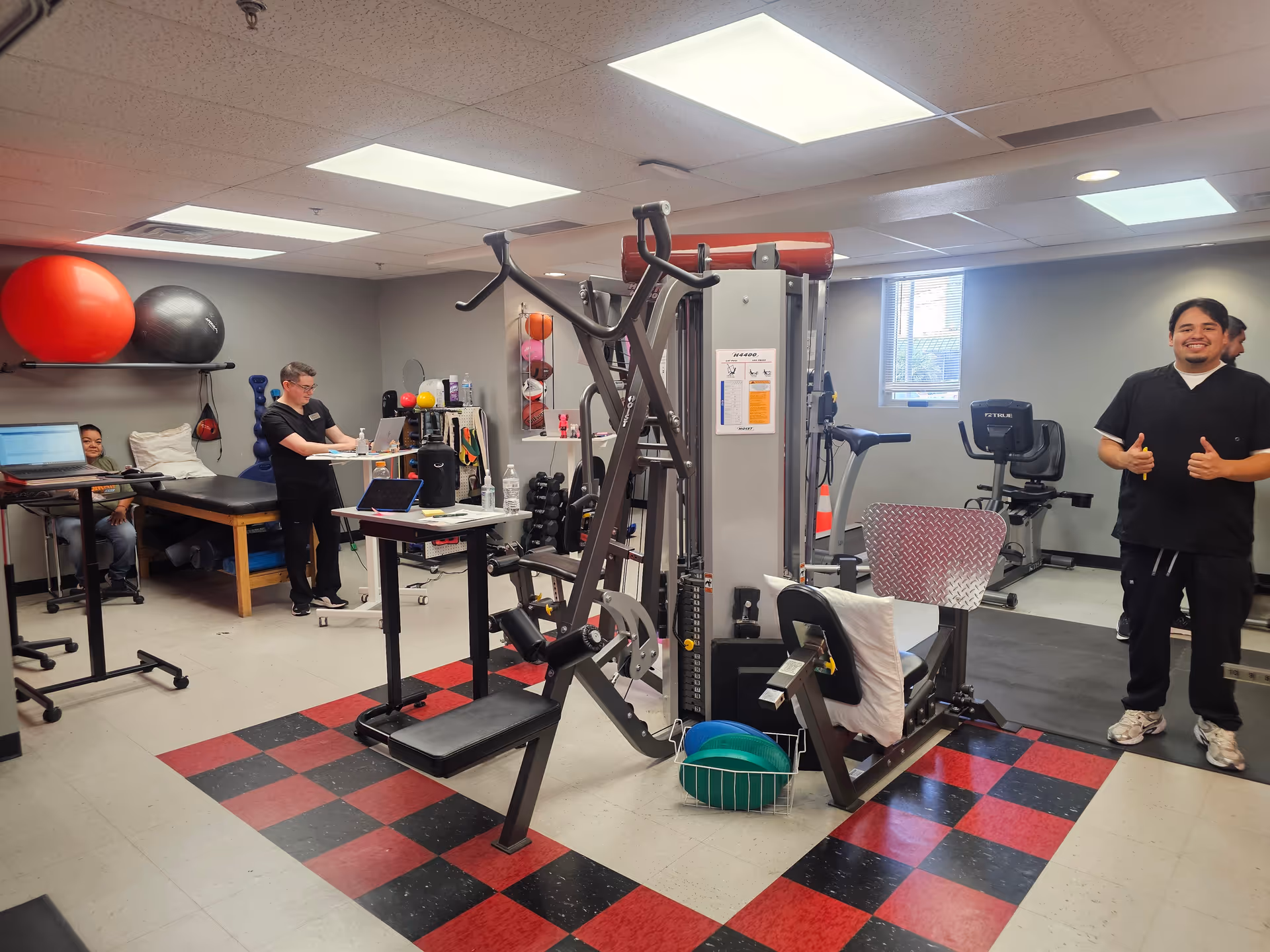 Indoor therapy gym with weight machines and staff standing near equipment.