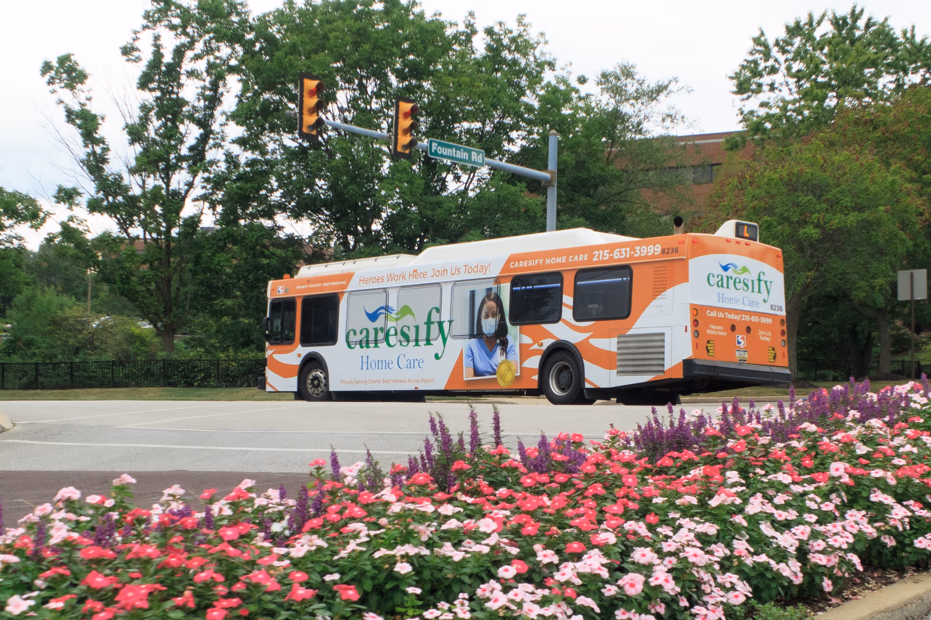 Orange and white Caresify Home Care bus parked along a street beside flowers.
