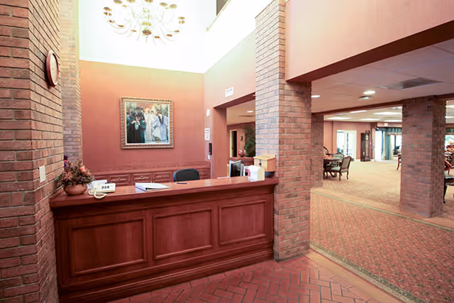 Reception desk in brick-walled lobby with chandelier, artwork, and seating area in the background.