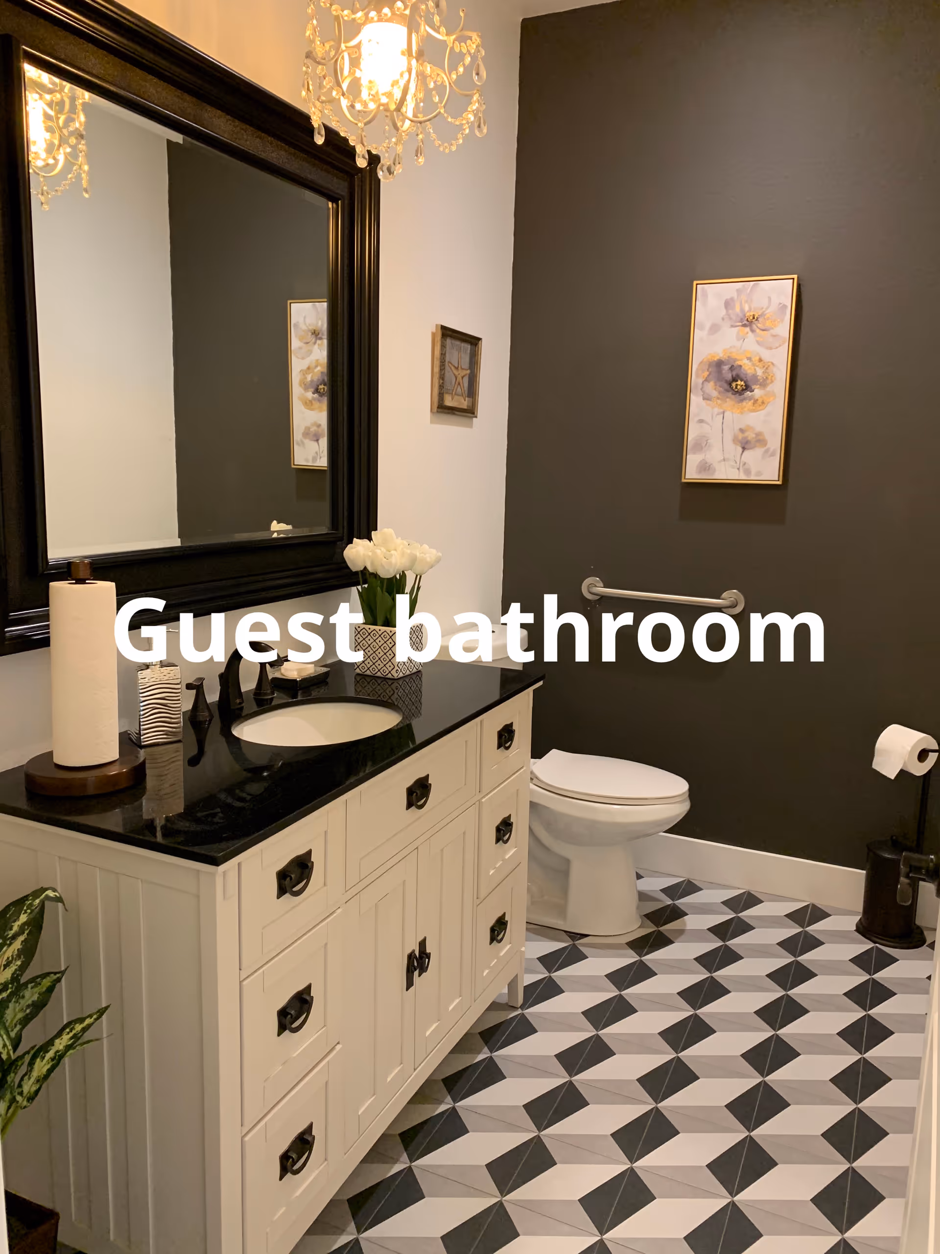 Guest bathroom vanity in a retirement home with black countertop, chandelier, and geometric tiled floor.