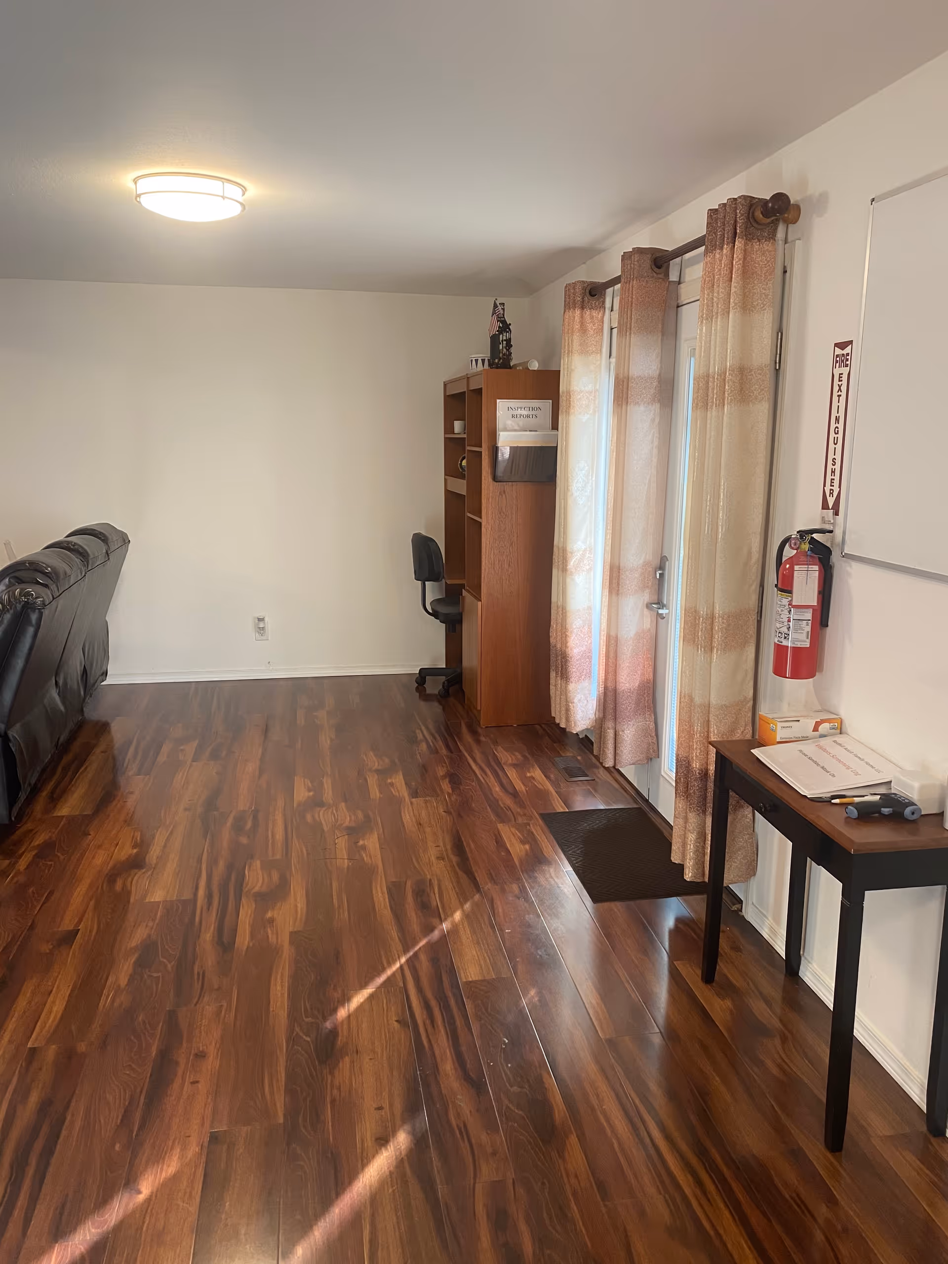 Living area with brown wood floor, couch, desk, bookshelf, and curtains.