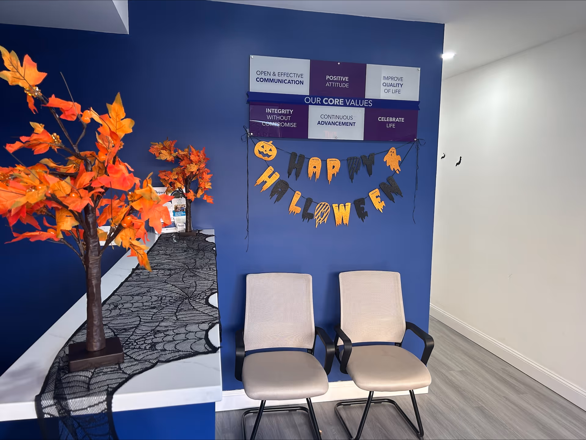 Blue-walled reception area with Halloween banner, two beige chairs, and autumn tree decor.