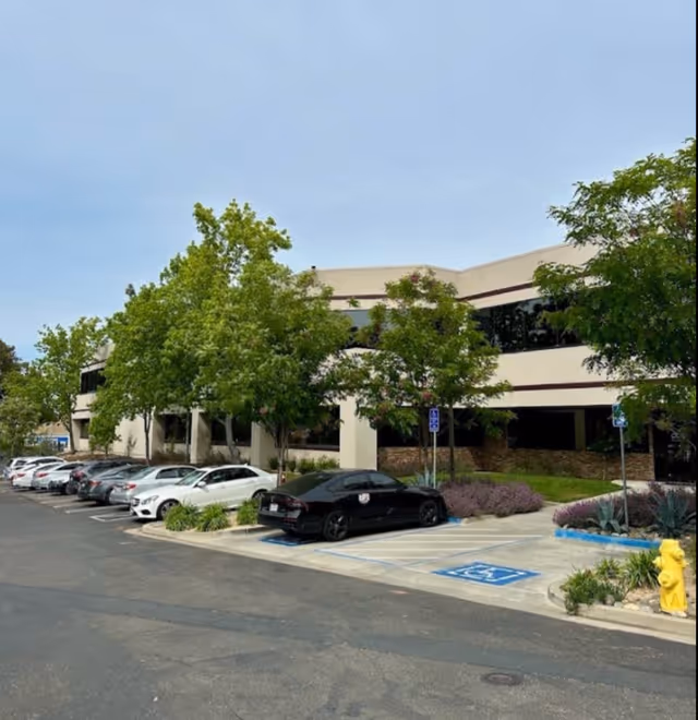 Exterior view of a senior living facility with parked cars and trees.