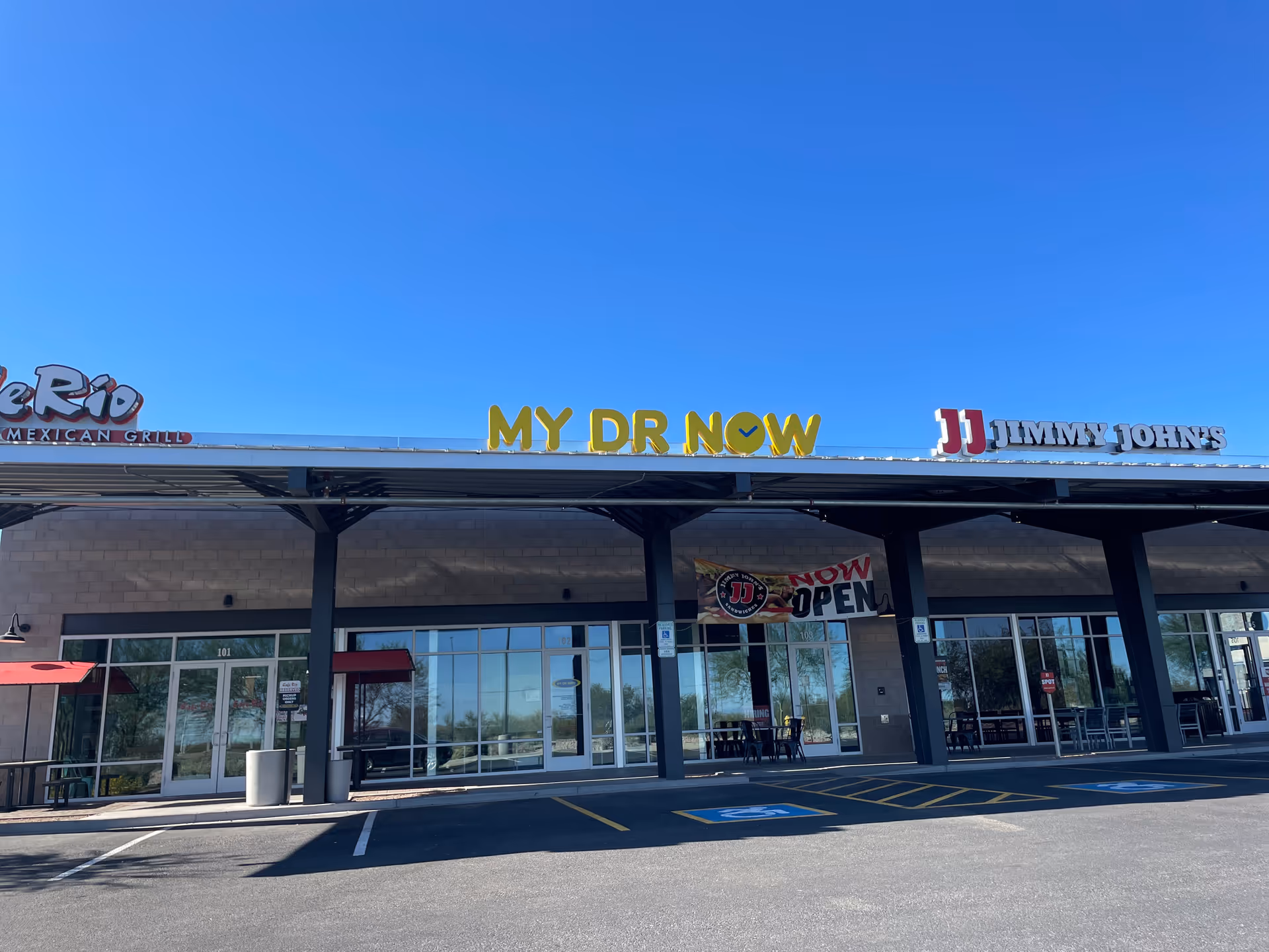 Exterior storefronts with MY DR NOW clinic between fast-food restaurants in a strip mall.