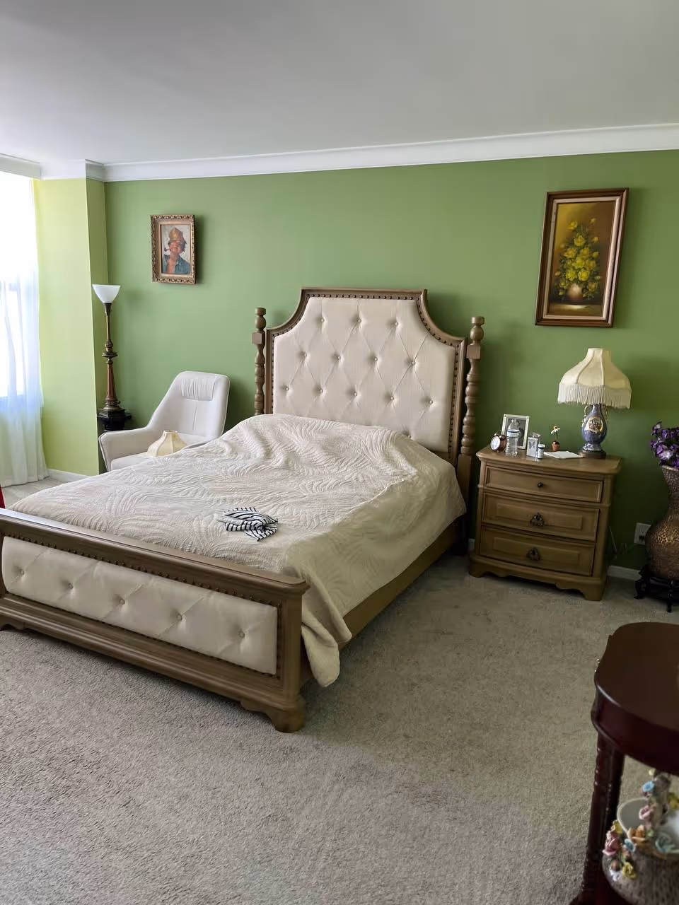 Green-walled bedroom featuring a tufted bed, nightstand, lamp, and framed artwork.