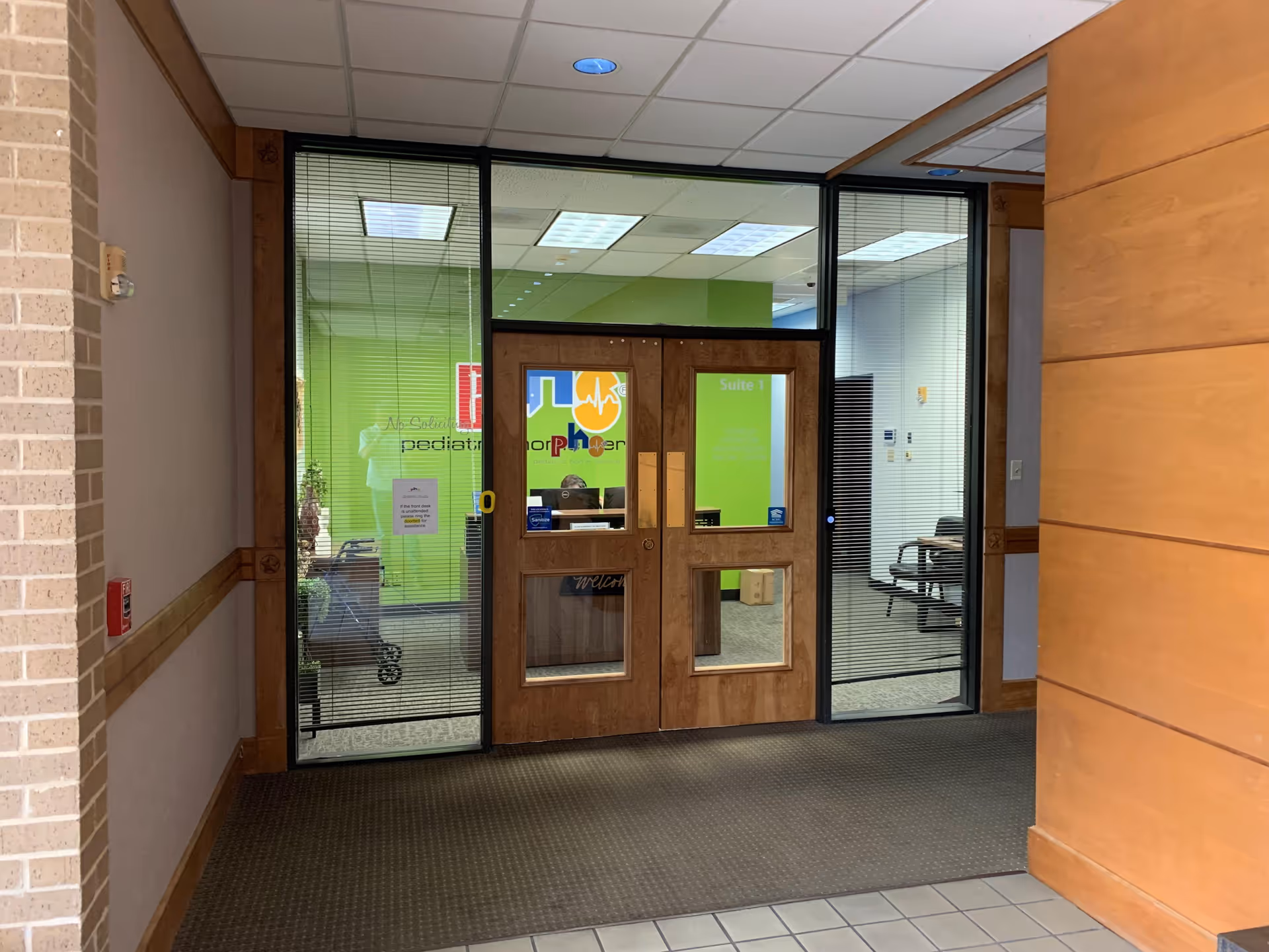 Wooden-framed glass doors open to a bright lobby with a Pediatric Home Service sign
