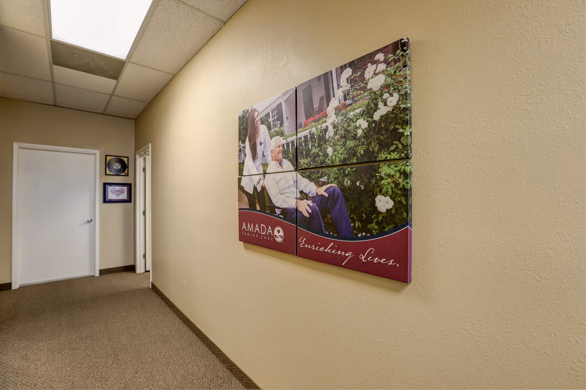 Interior hallway in Amada Senior Care with large wall art and multiple doors along beige walls.
