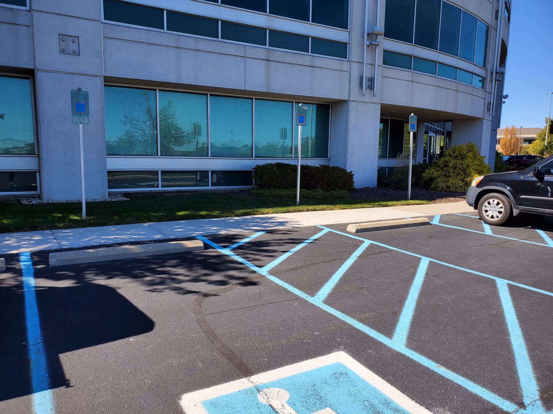 Exterior view of a modern facility with blue handicap parking spaces and shrubs.