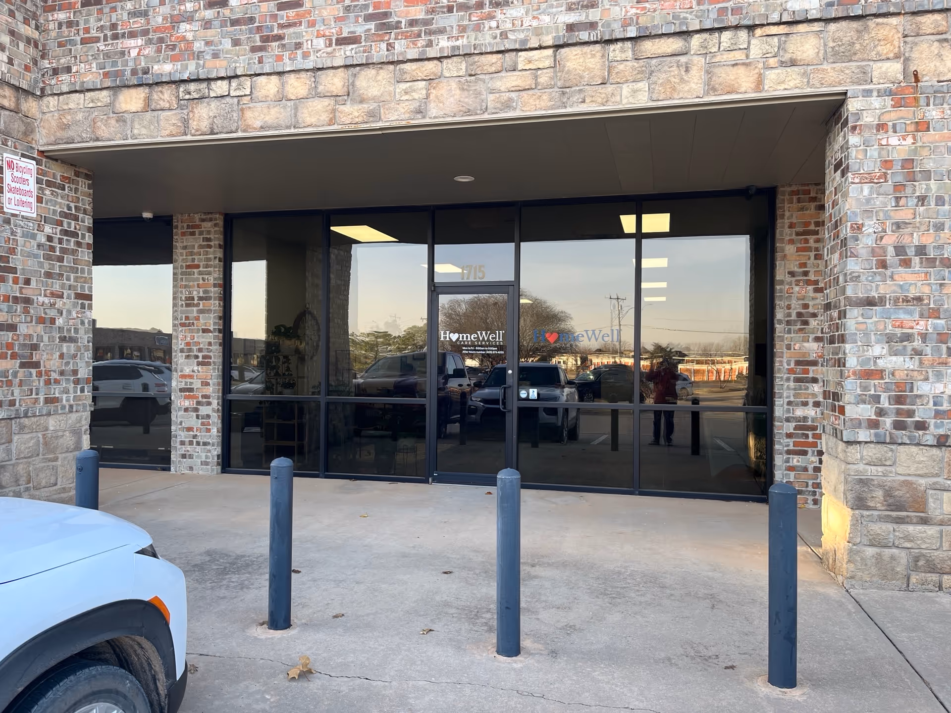 Brick building entrance with glass doors labeled HomeWell Care Services and a parking lot.