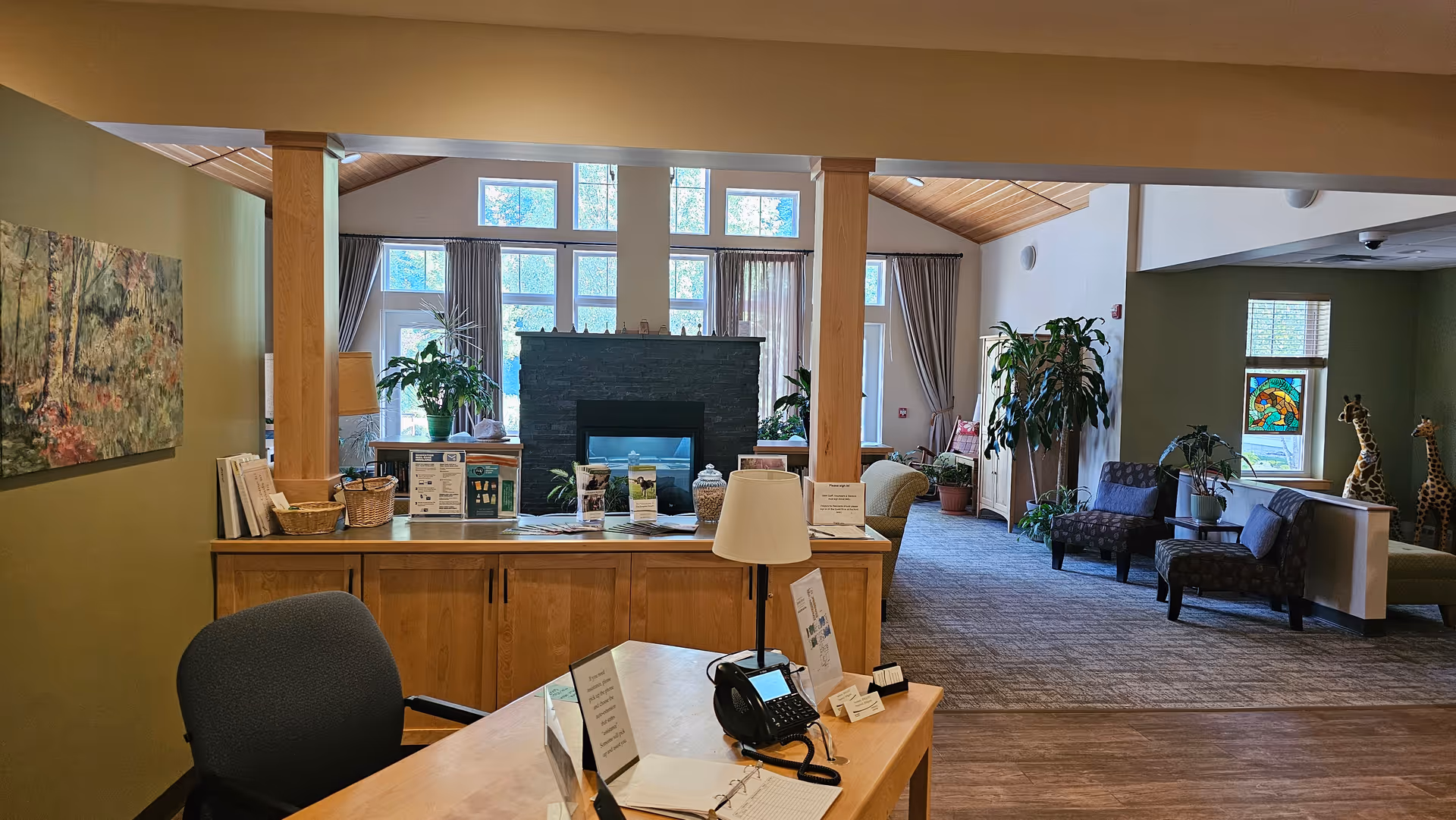 Reception desk in a warm lounge with seating, plants, and a fireplace.