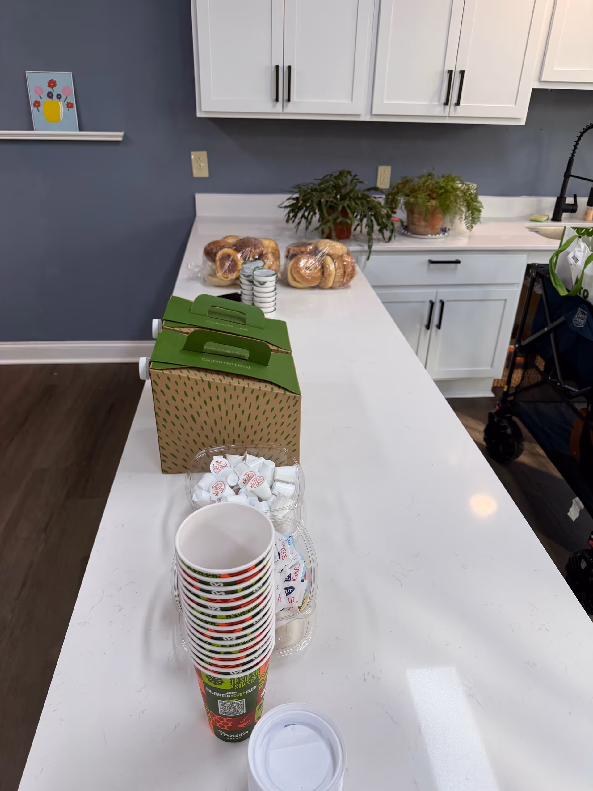 Long white kitchen counter with cups and pastries against blue walls.