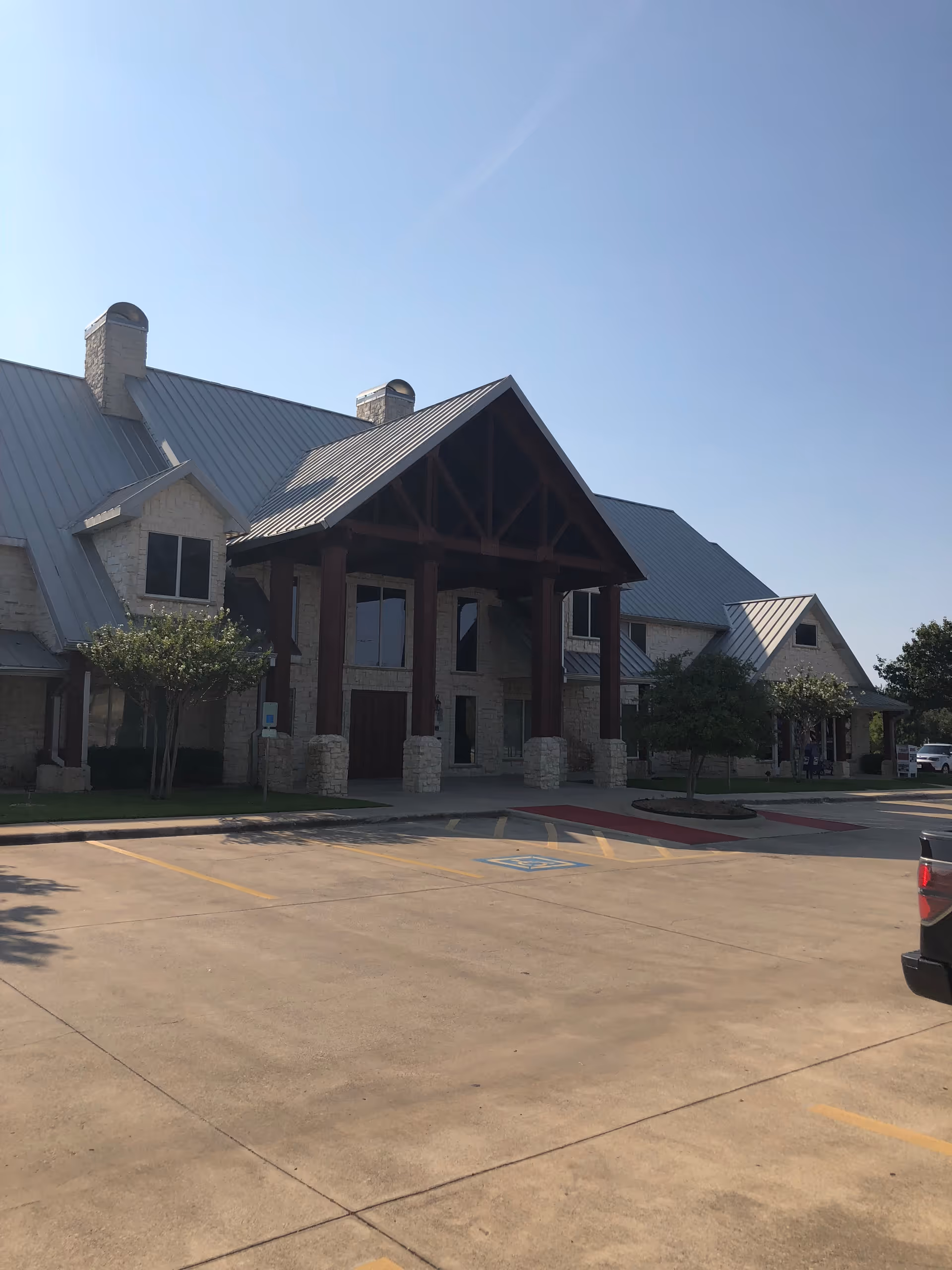 Senior living facility exterior with stone pillars, metal roof, and a covered entrance.