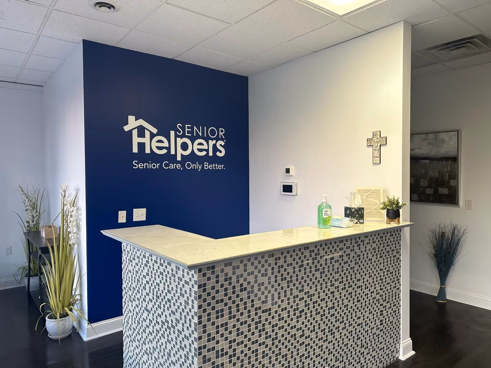 Reception desk inside Senior Helpers Upstate facility with blue logo wall and tiled counter.