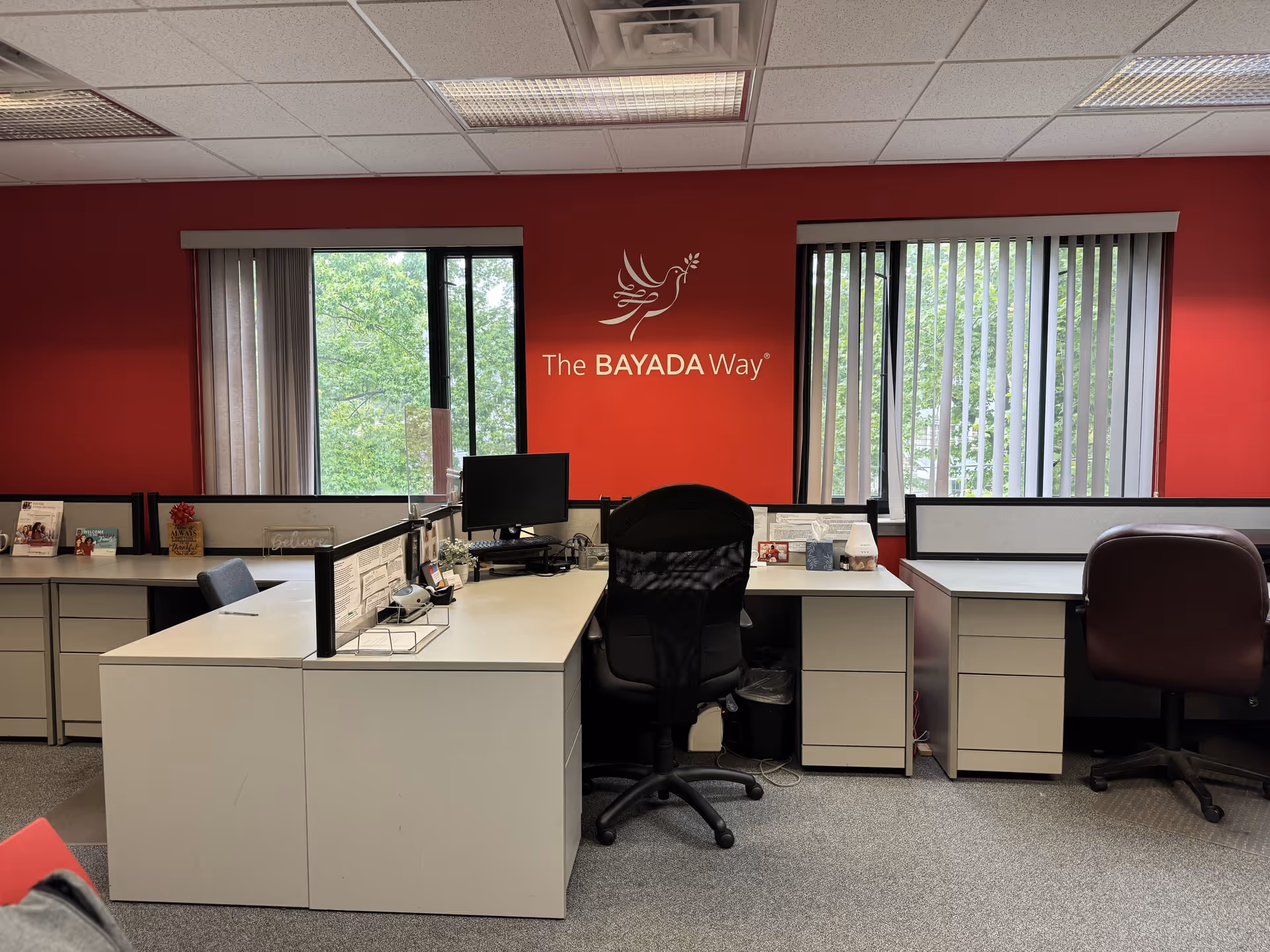 Office reception area with cubicles and a red wall displaying The BAYADA Way logo.