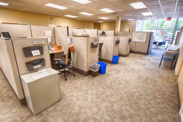 Row of cubicles and desks in a spacious administrative office area inside a senior care facility.