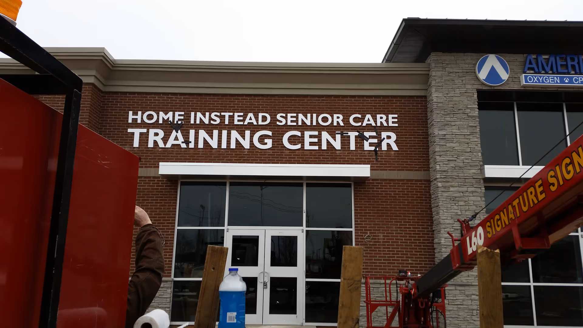 Brick exterior of Home Instead Senior Care Training Center with glass doors and a lift nearby.