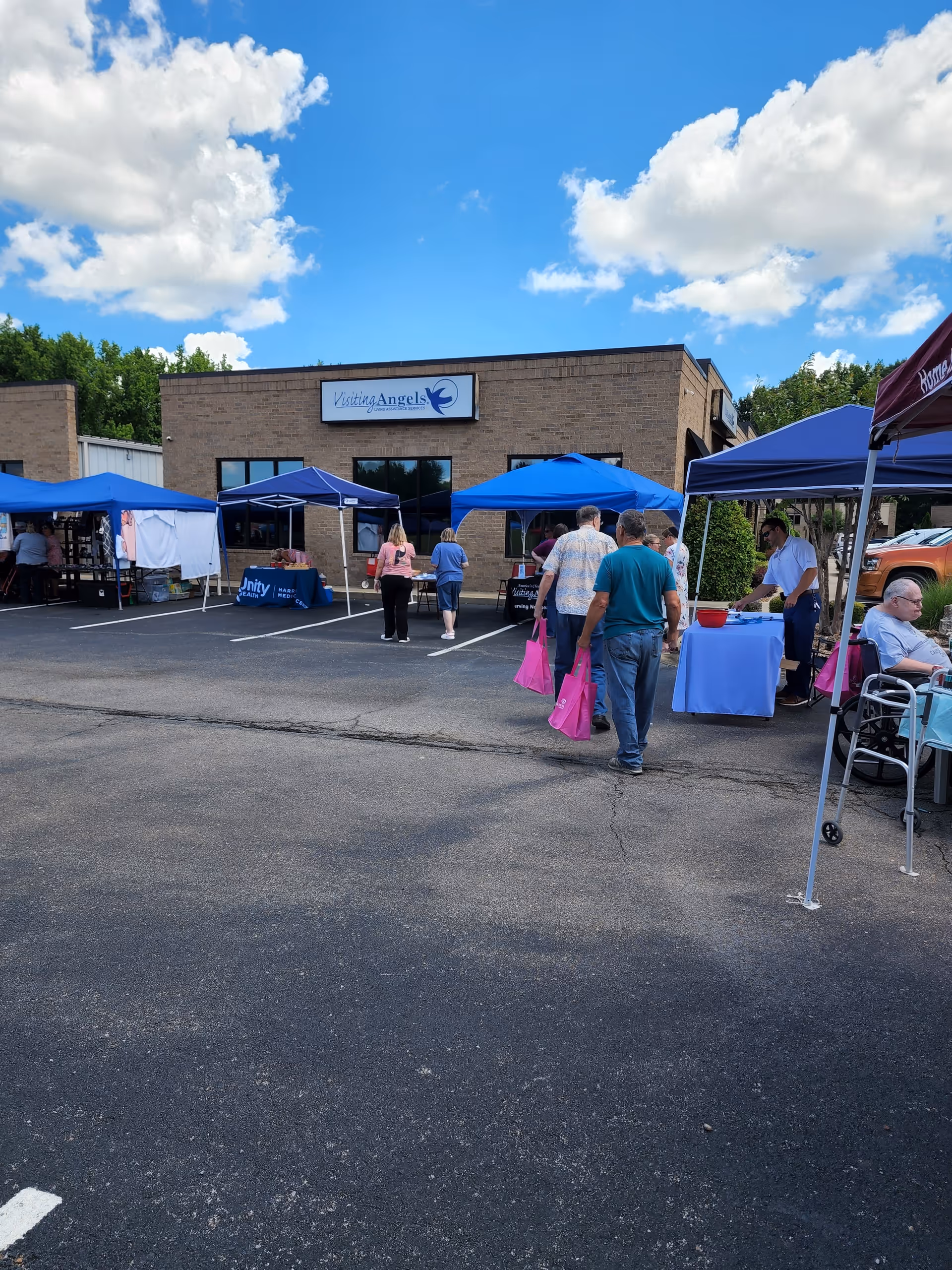 Exterior view of Visiting Angels Senior Home Care with blue outdoor tents and people walking outside.