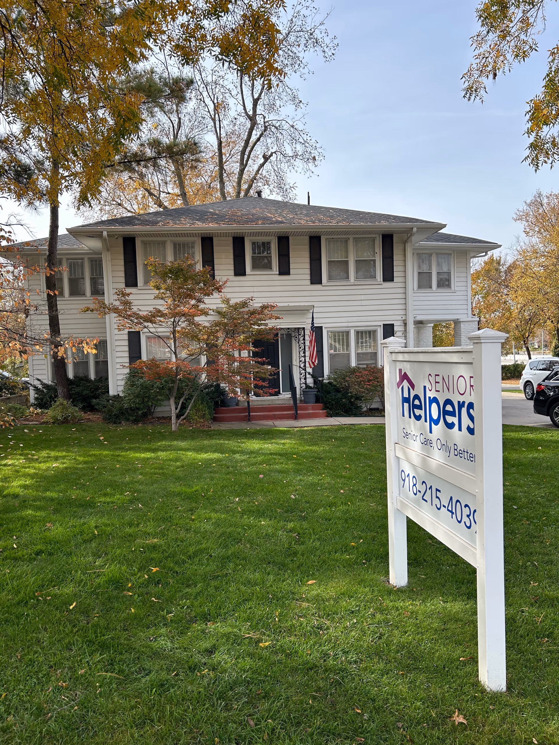 Two-story white building with black shutters and a prominent Senior Helpers sign on the lawn.