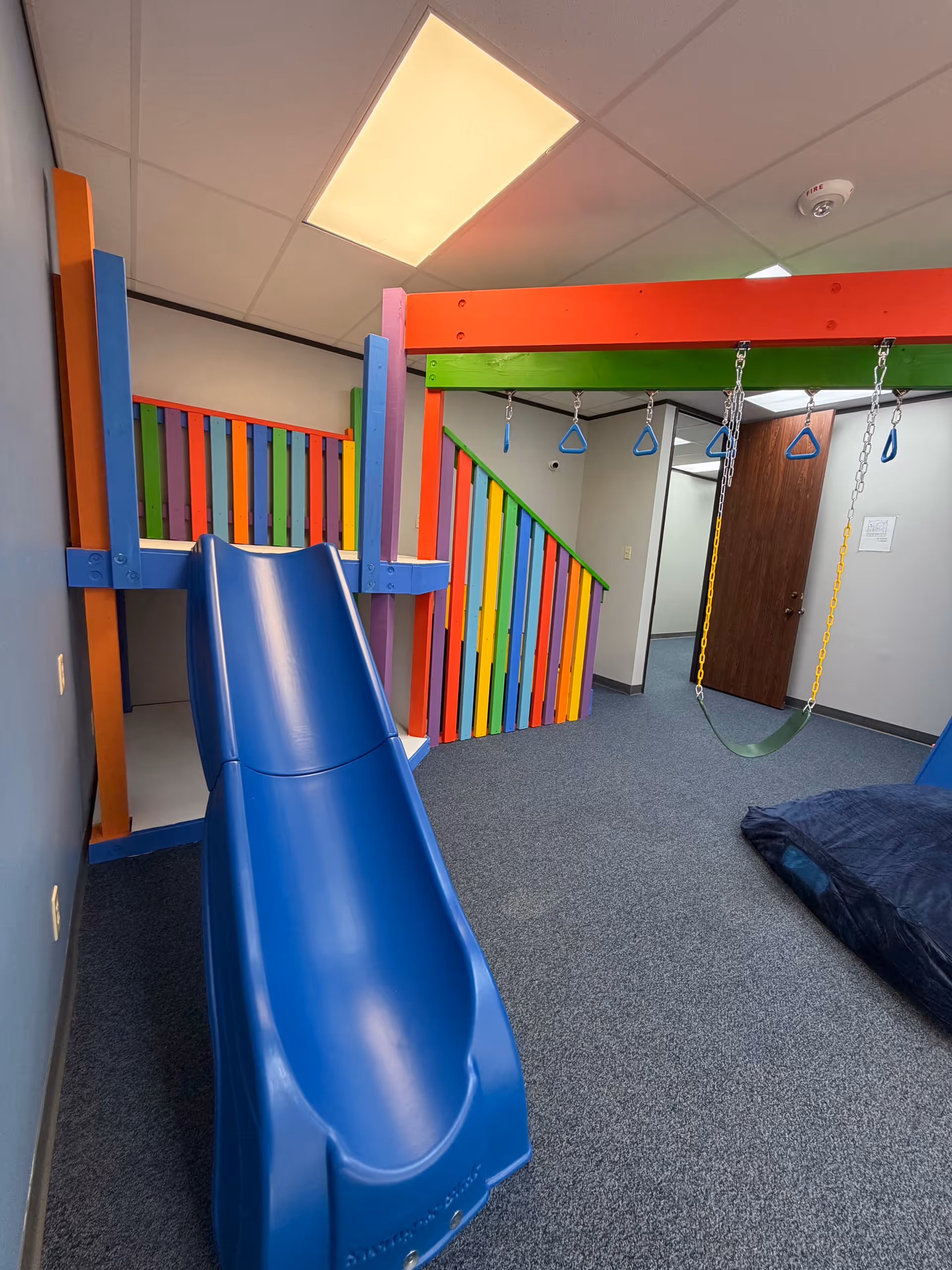 Colorful indoor play area with a blue slide and climbing structures.