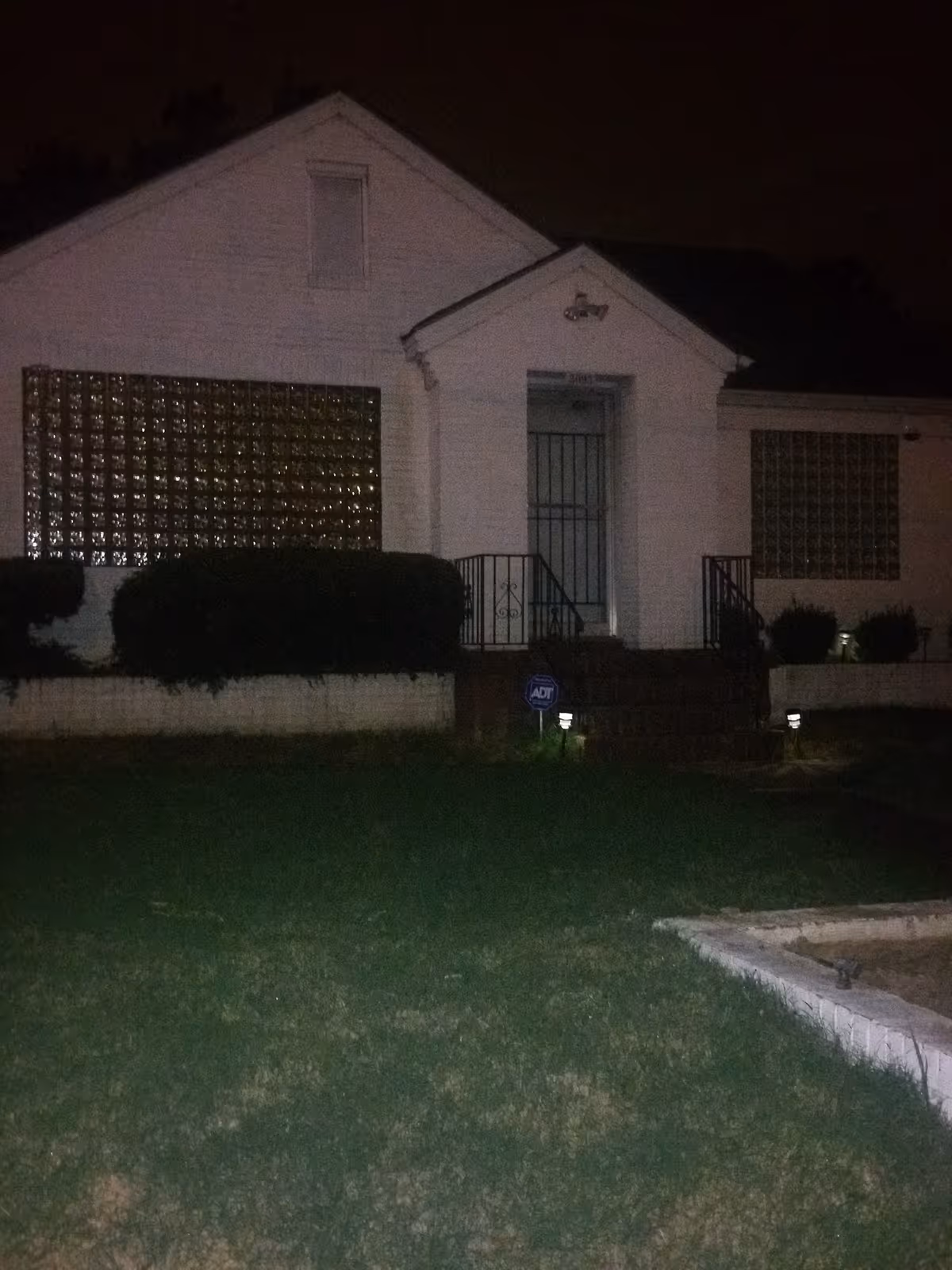 Nighttime exterior of a small white building with steps and gated entrance