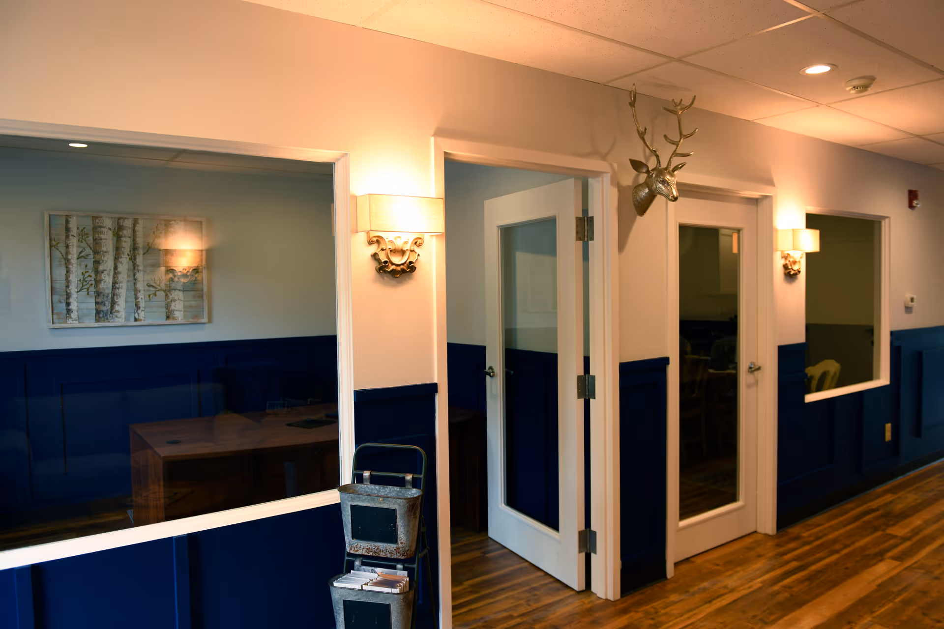 Interior corridor in a facility featuring blue wainscoting, doors, and a deer head mount.