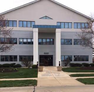 Two-story light-gray building with a central entrance, walkway, and planters.