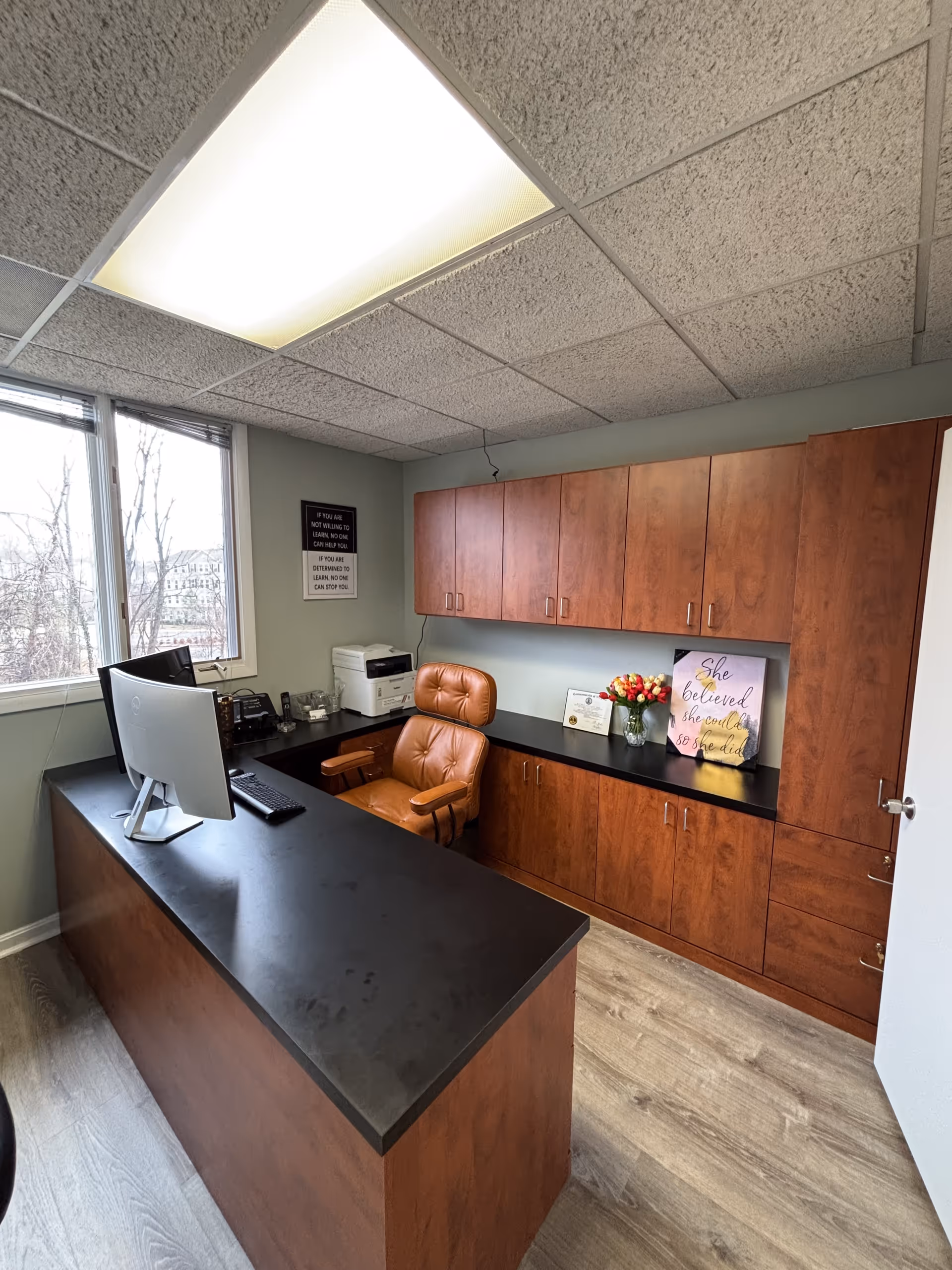 Office space in Mazeno Healthcare with a desk, chair, computer, printer, and wooden cabinets.