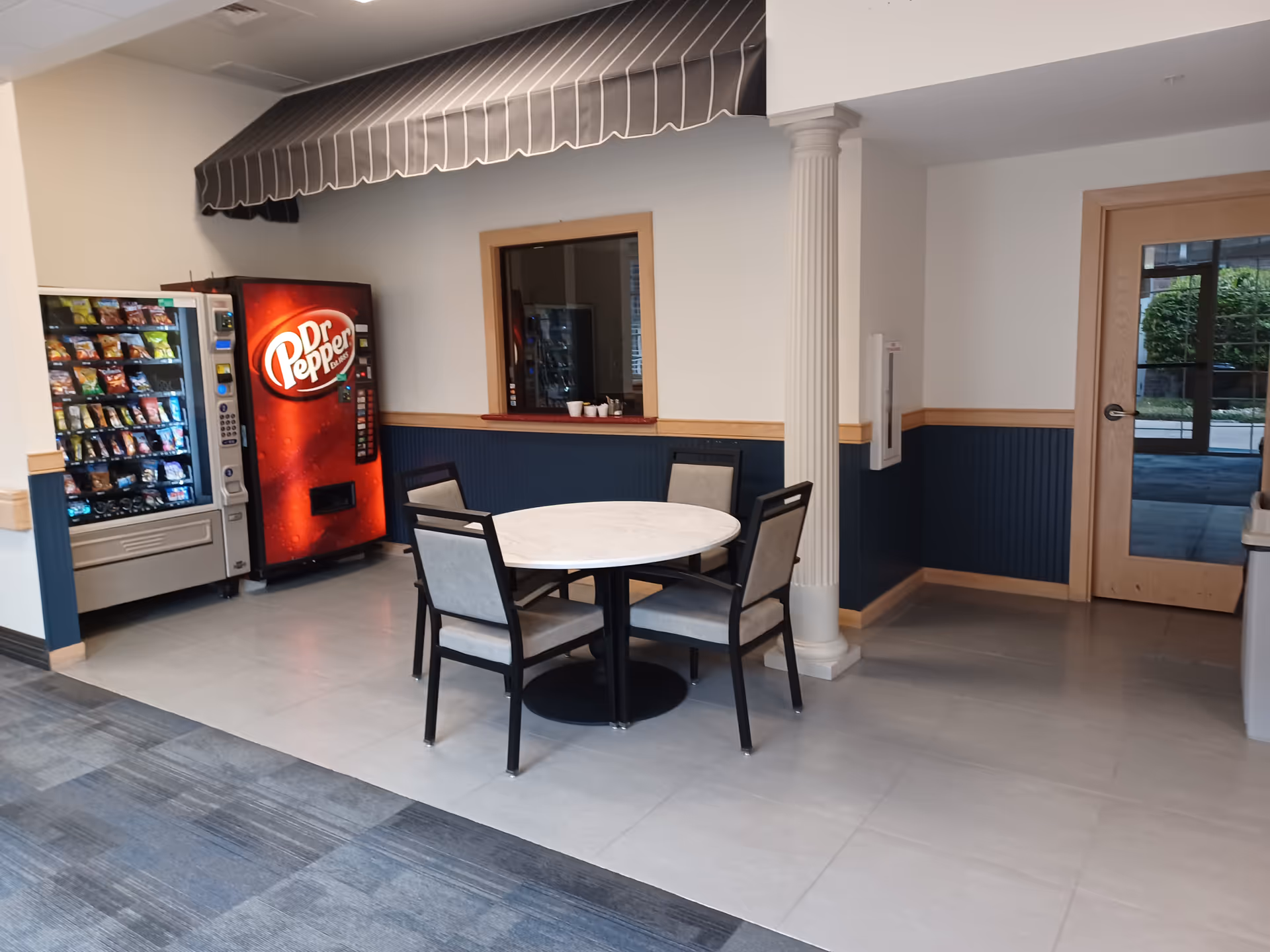 Interior lobby area with vending machines, a round table, chairs, and a doorway.