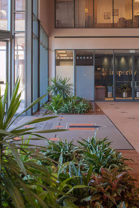 Spacious lobby with glass doors, potted plants, and a tiled walkway.