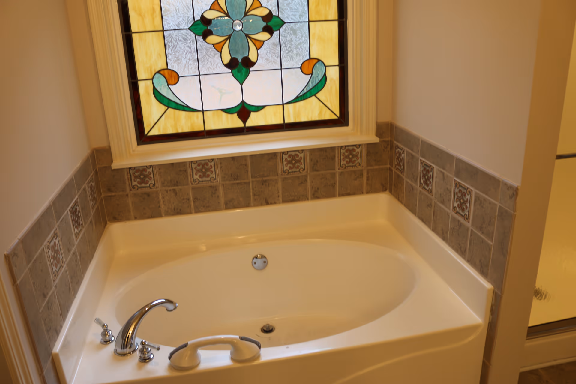 A bathroom with a white tub, tiled walls, and a stained glass window.