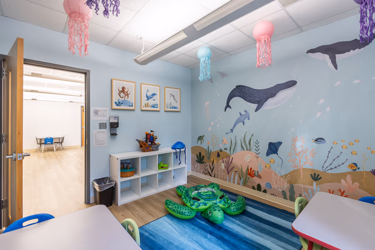 Colorful children's playroom with ocean mural, cubbies, and small tables inside a facility.