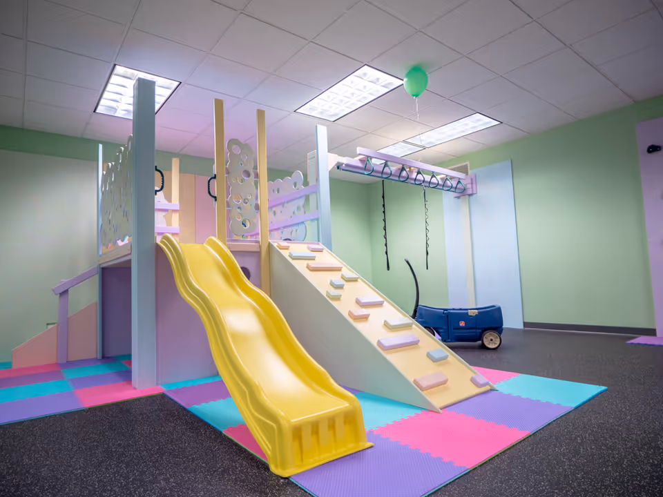 Colorful indoor play structure with a yellow slide and padded flooring in a playroom