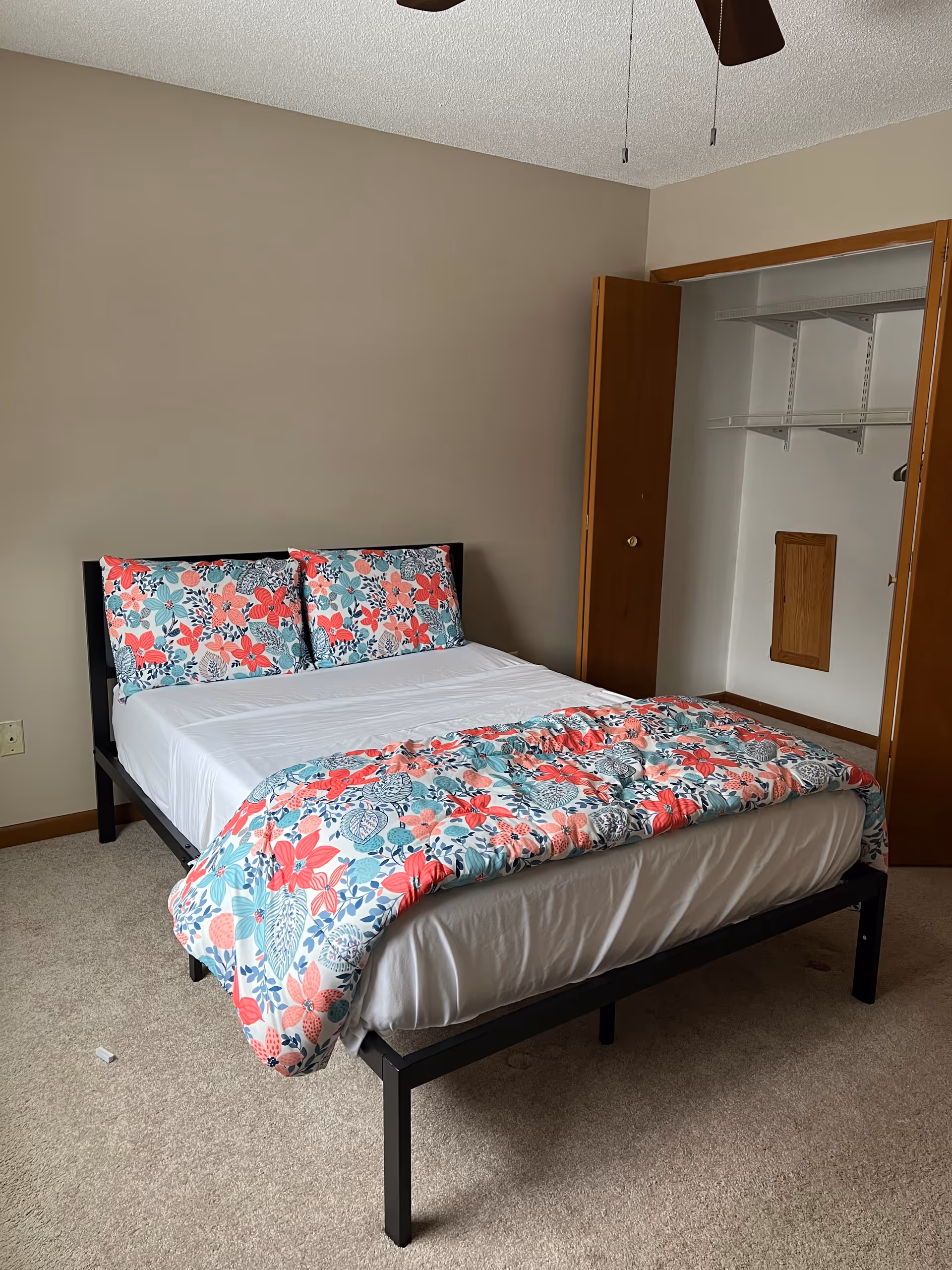A neatly made bedroom with floral bedding and an open closet.
