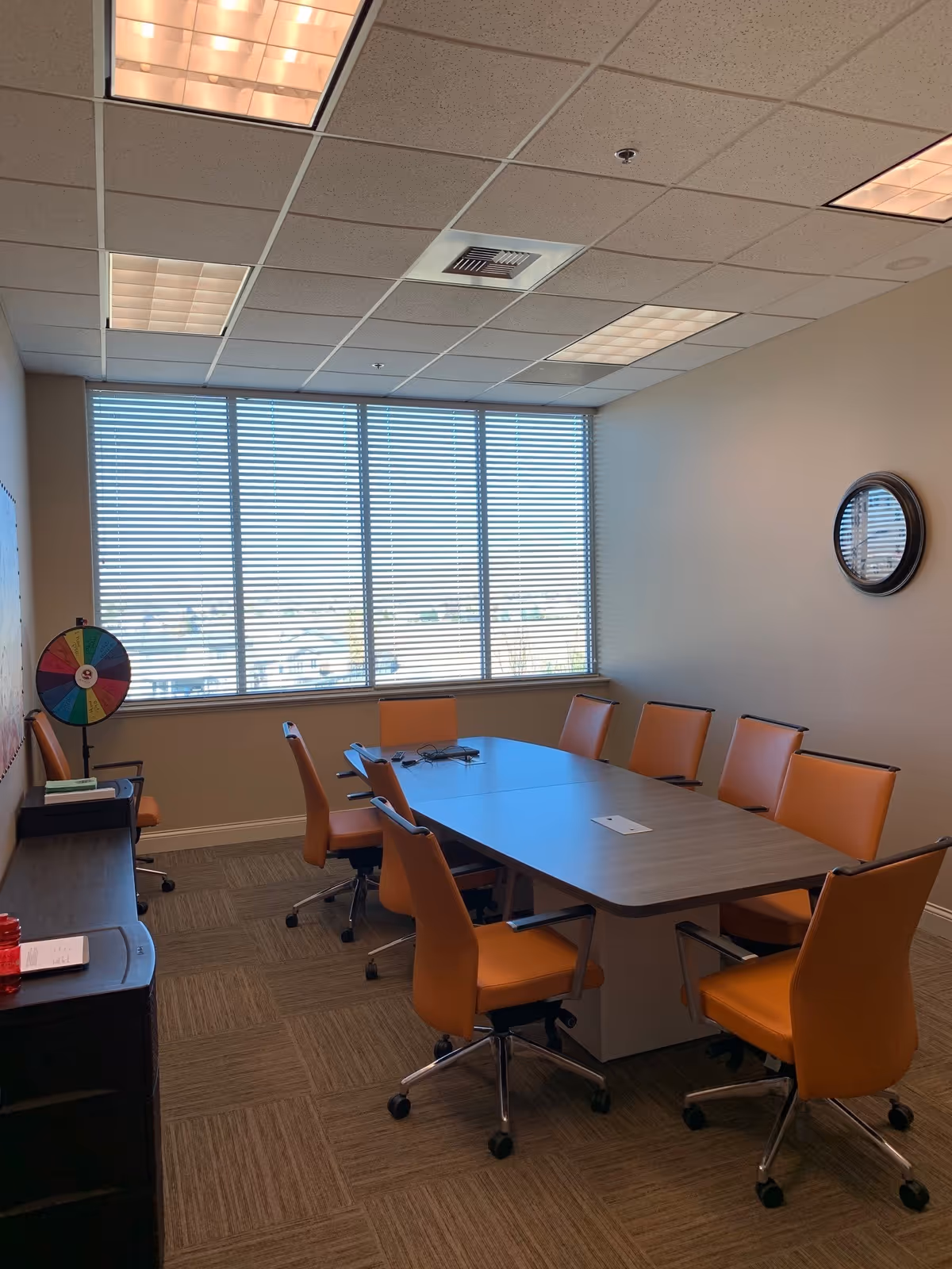 Bright meeting room with orange chairs around a large table by window blinds.