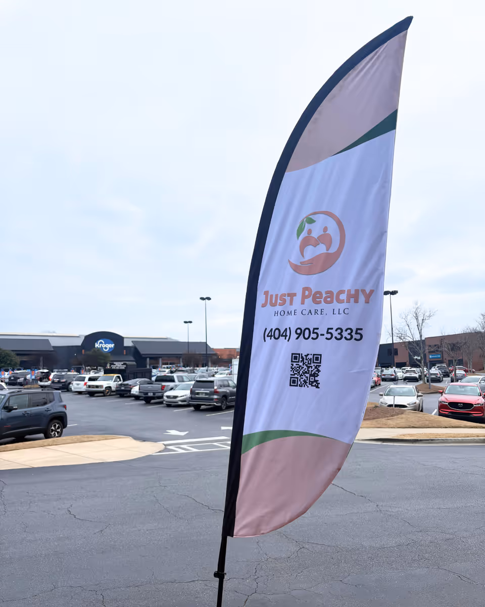Flag banner for Just Peachy Home Care LLC in a parking lot outside.