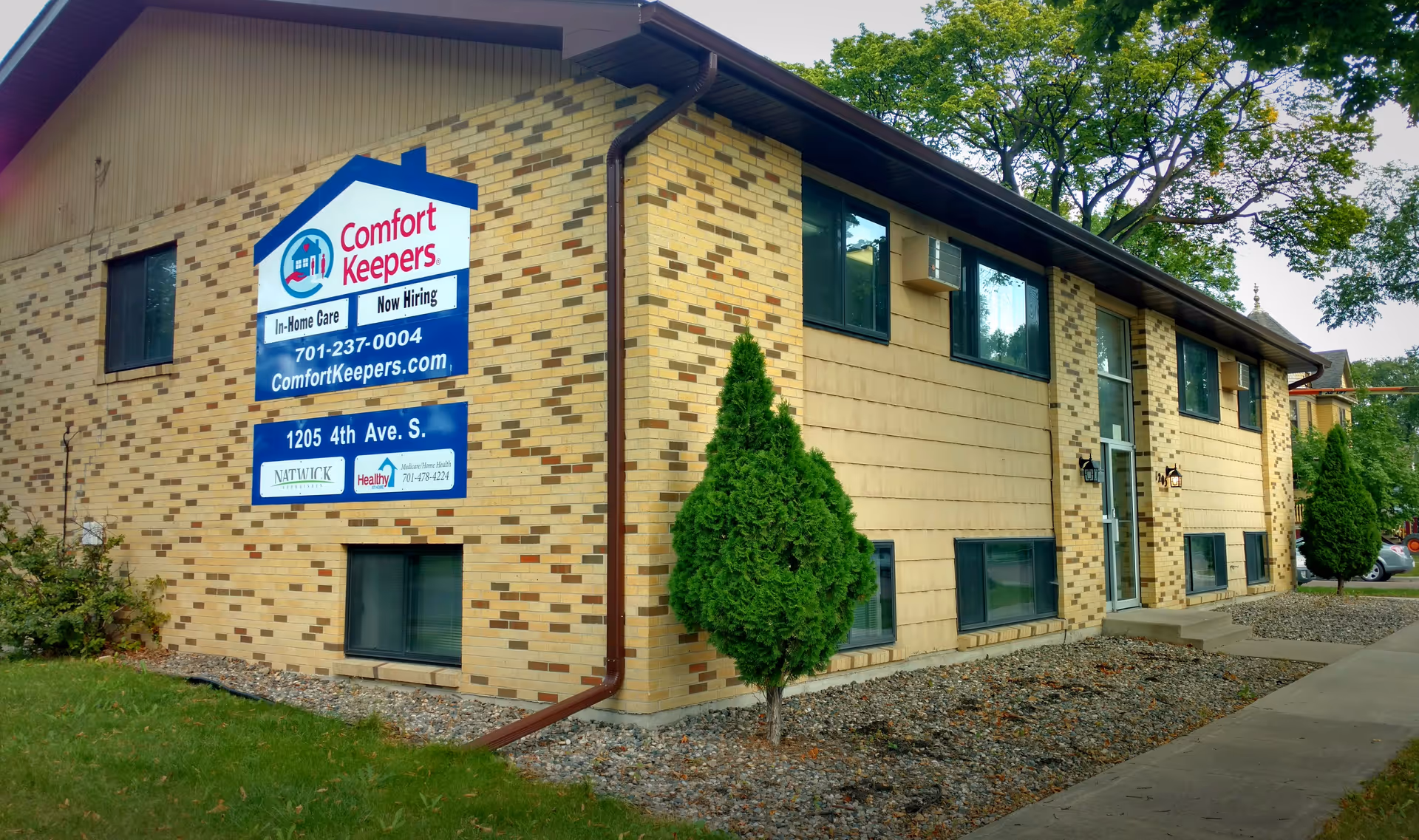 Two-story brick senior living facility with Comfort Keepers sign and landscaped front yard.