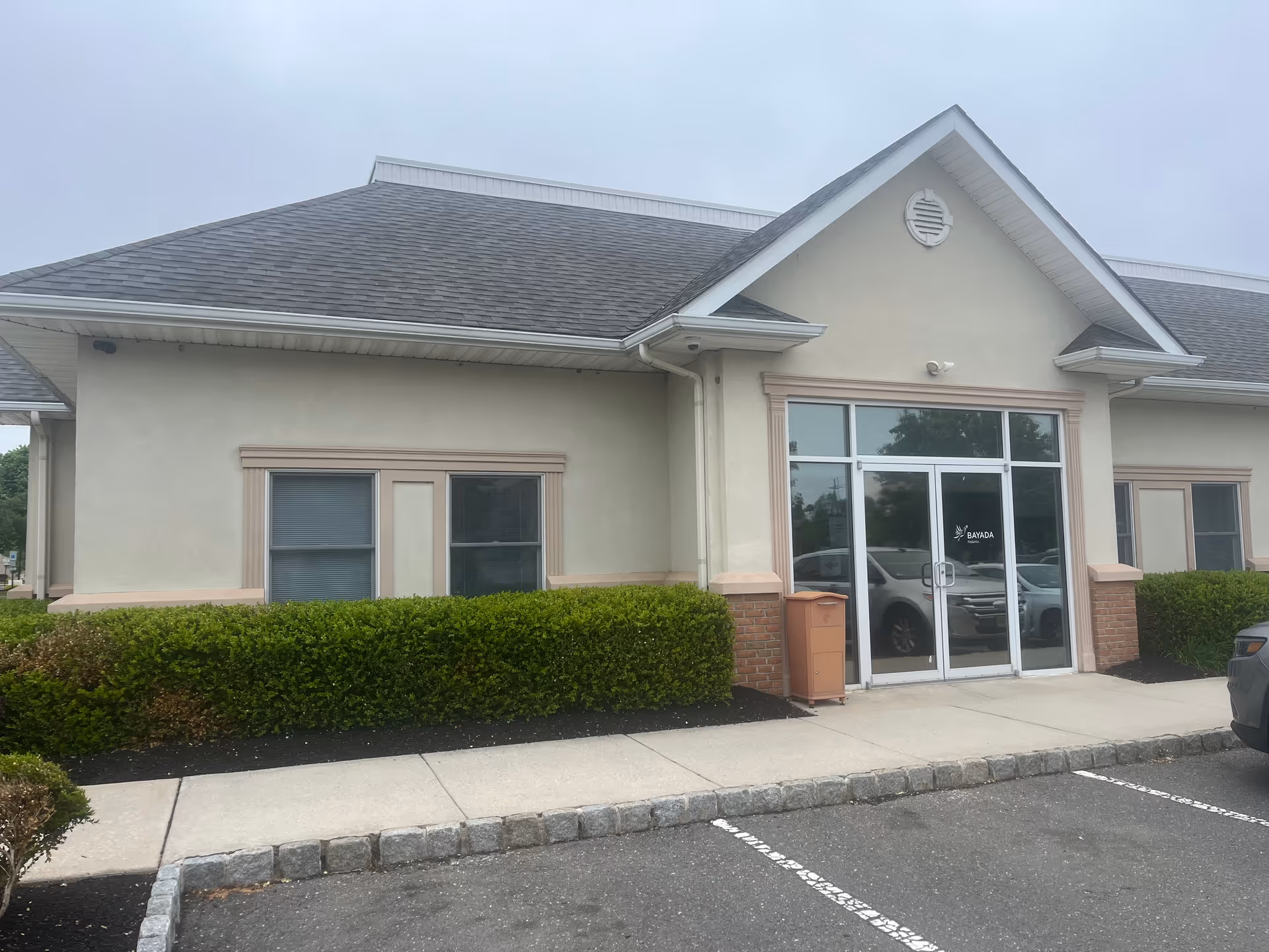 Exterior view of a BAYADA Pediatrics building entrance with glass doors and hedges.