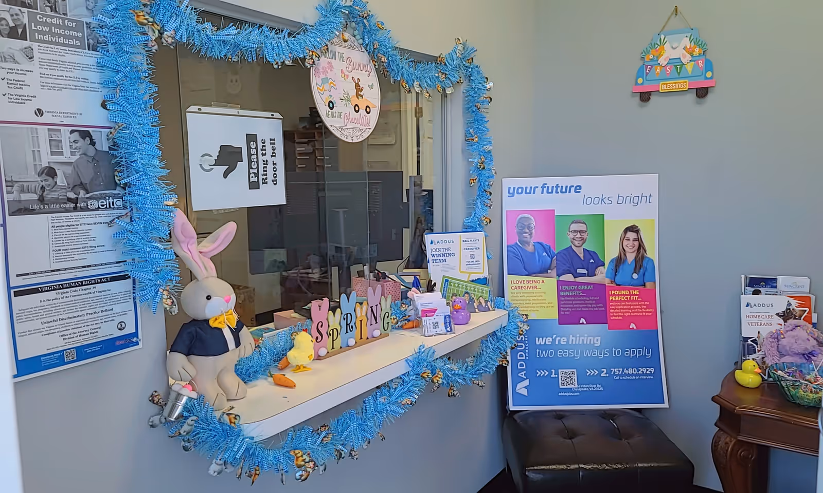 Interior reception window decorated with blue tinsel, Easter bunny plush, and hiring posters.