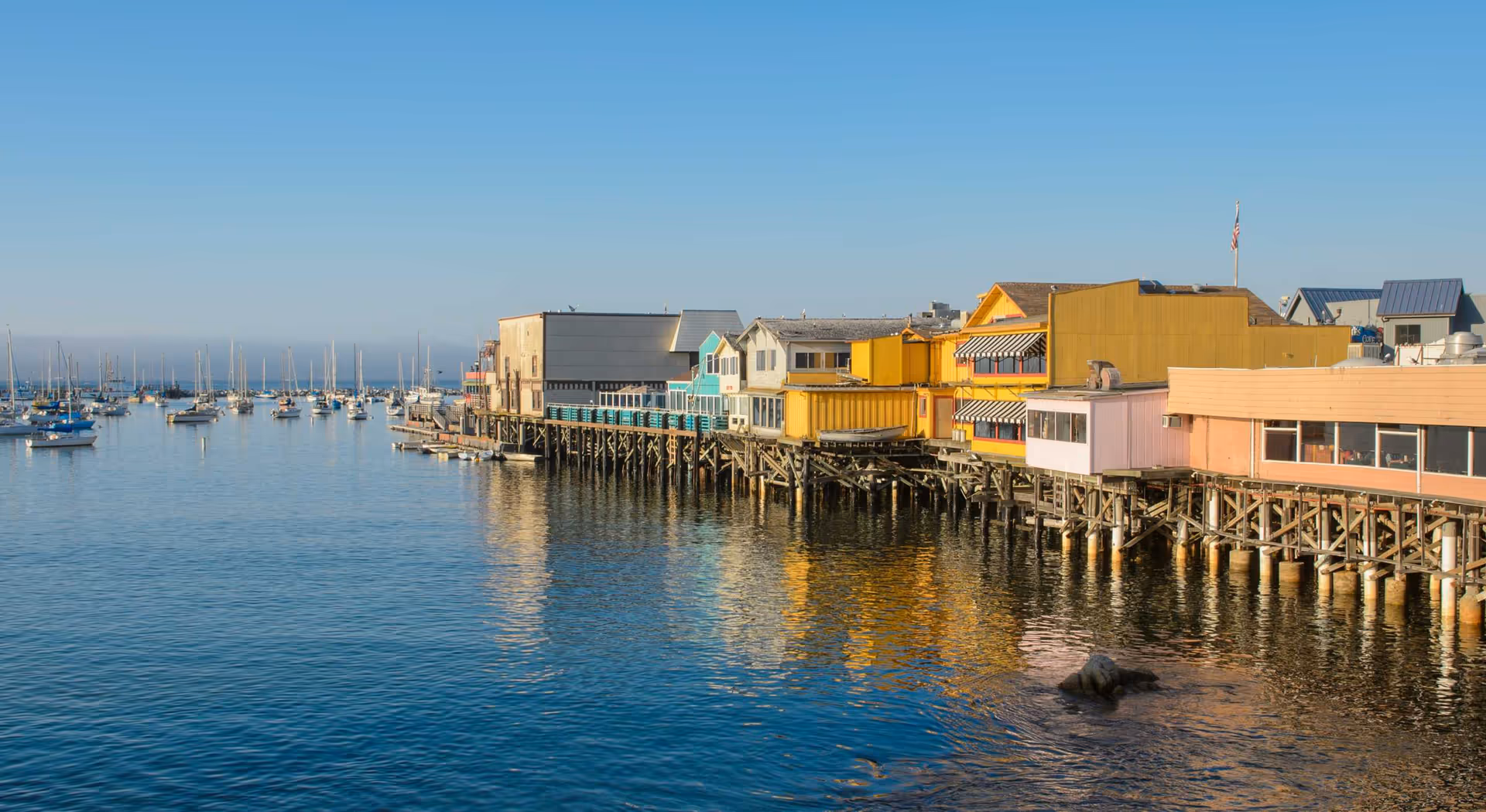 Colorful waterfront buildings on stilts along calm harbor with boats.