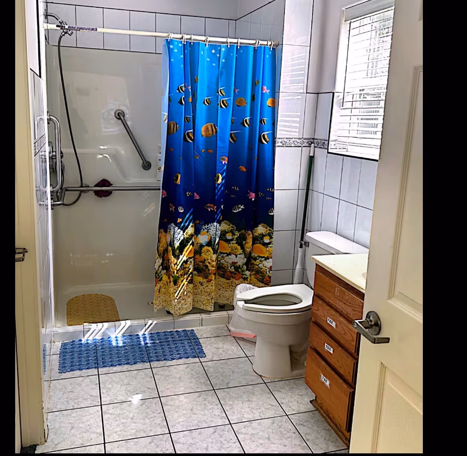 Small bathroom with a blue fish-themed shower curtain, toilet, sink, and tiled floor.