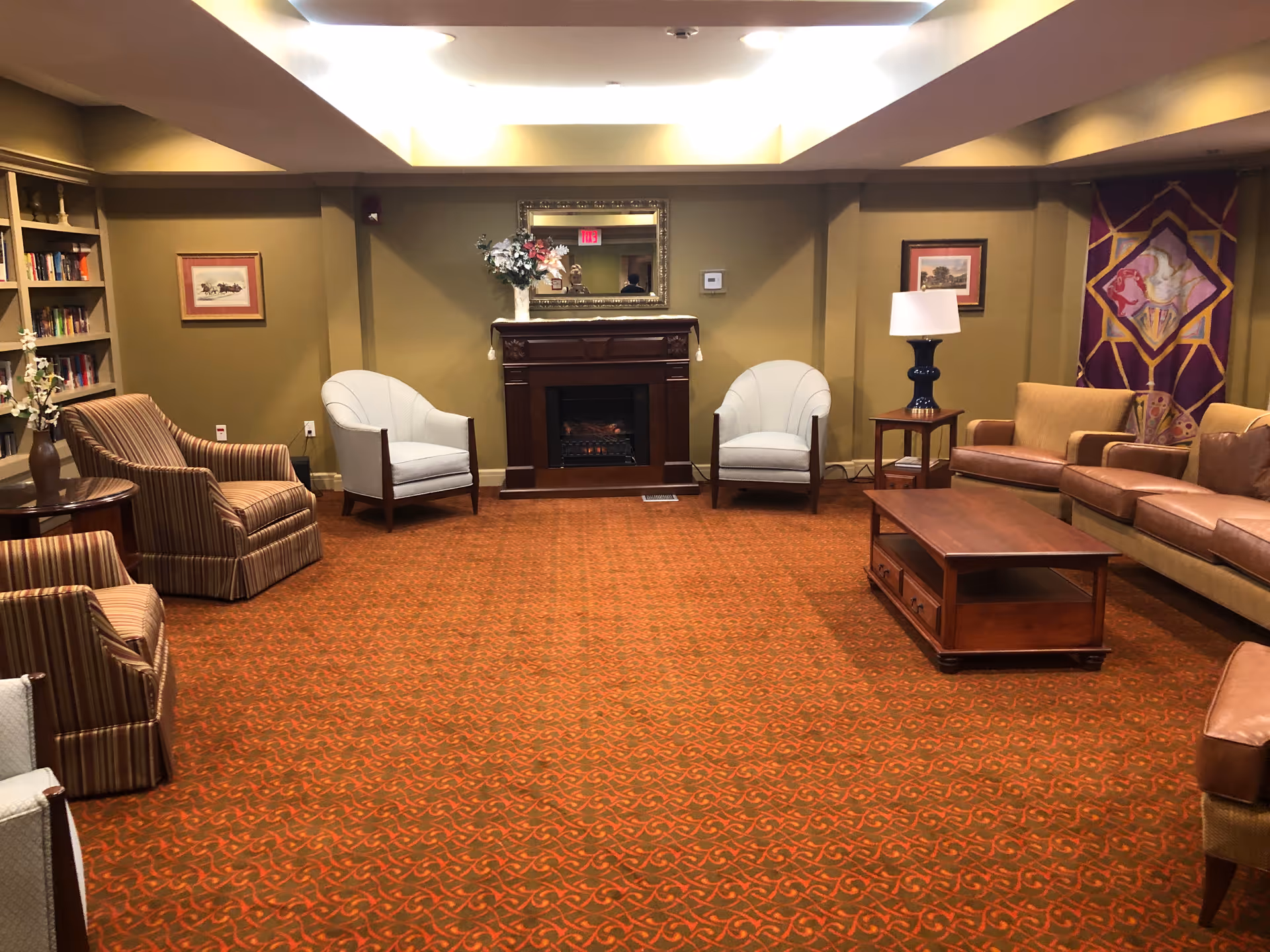 A cozy communal living room with sofas, chairs, fireplace, and warm decor in a senior facility.