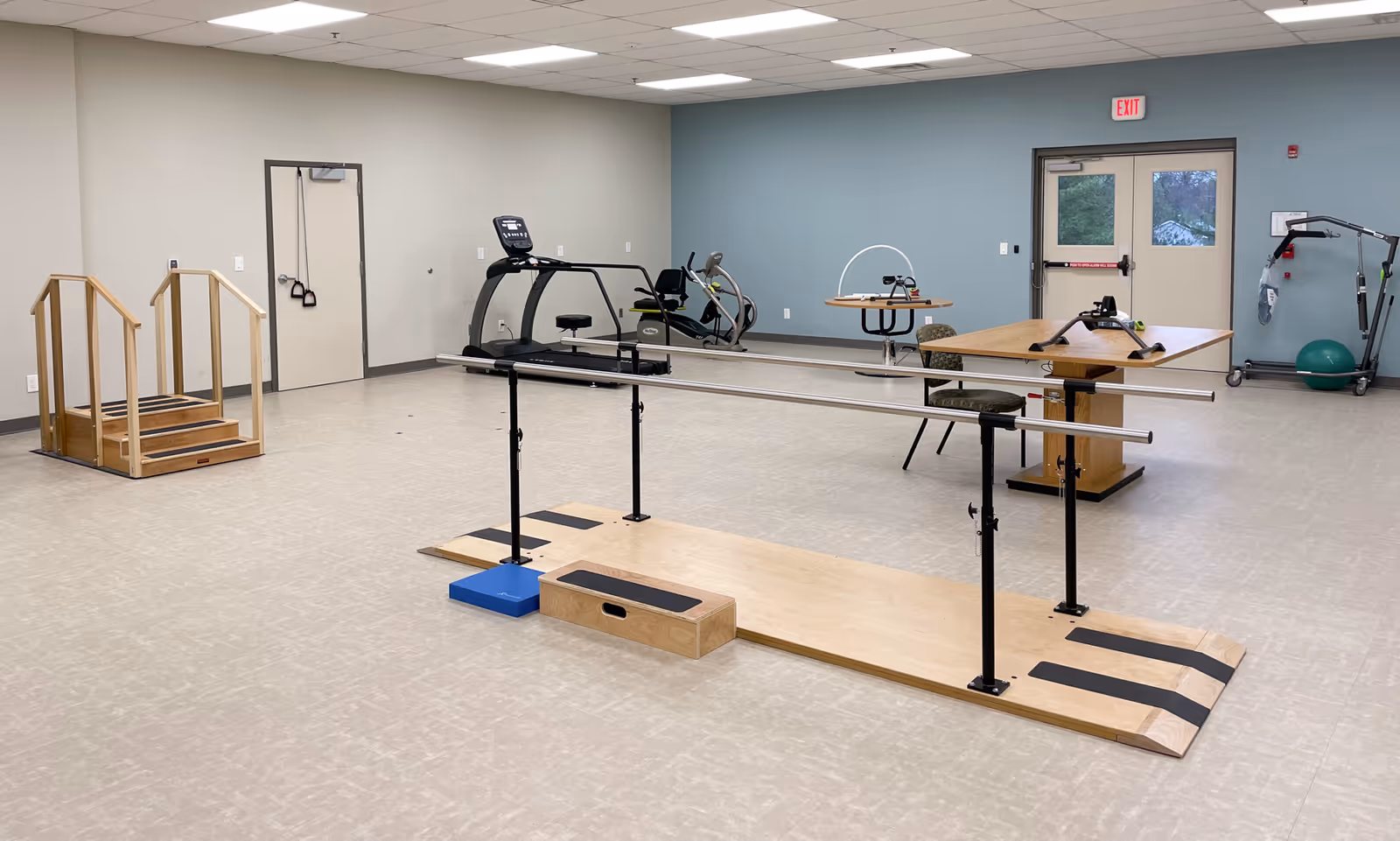 Interior rehab gym with parallel bars, treadmills, balance beam, and equipment in a senior facility.